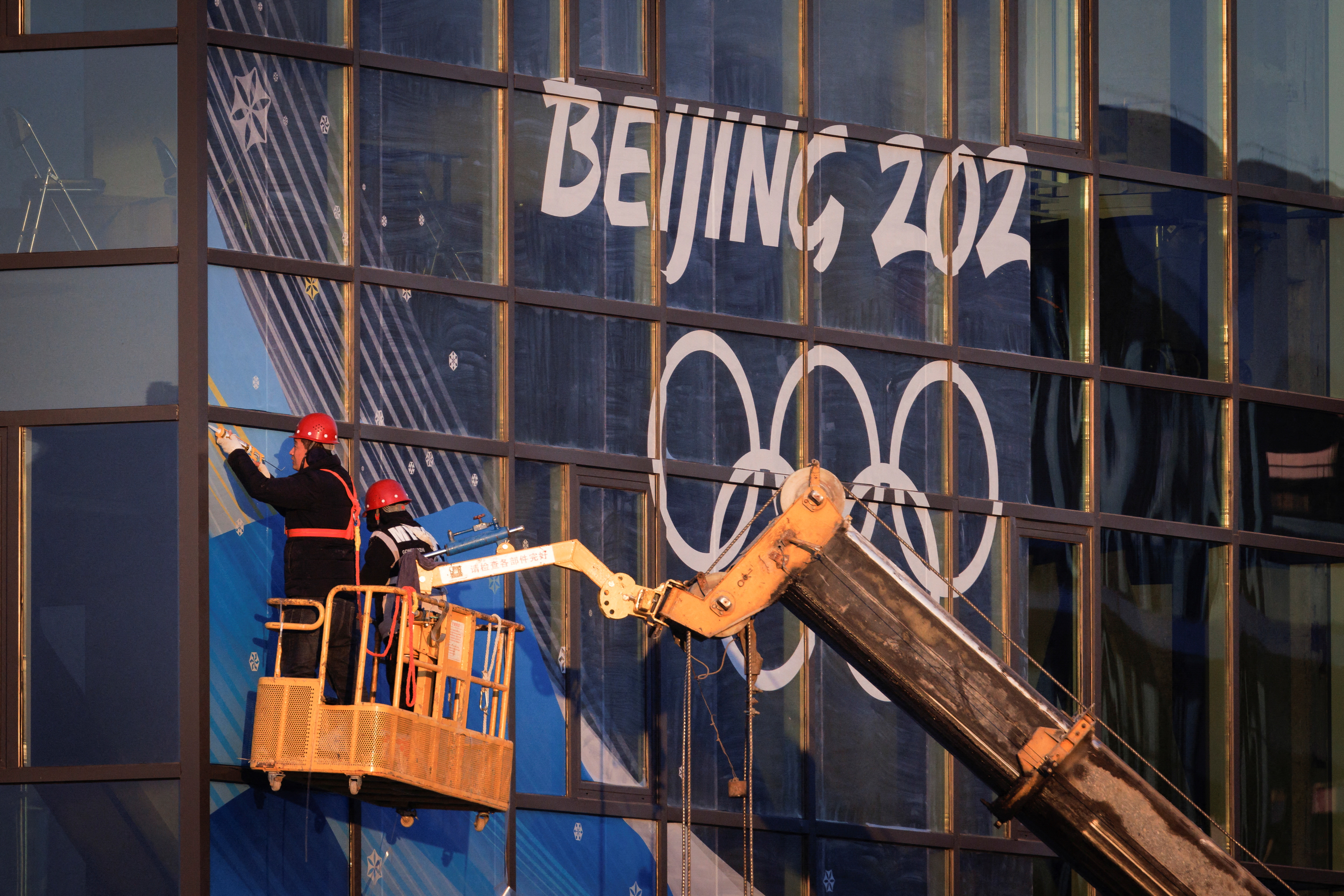 Workers attach signage near Big Air Shougang, a competition venue for the Beijing 2022 Winter Olympics, at Shougang Park, the site of a former steel mill, in Beijing, China, December 28, 2021. Picture taken December 28, 2021.  REUTERS/Thomas Peter