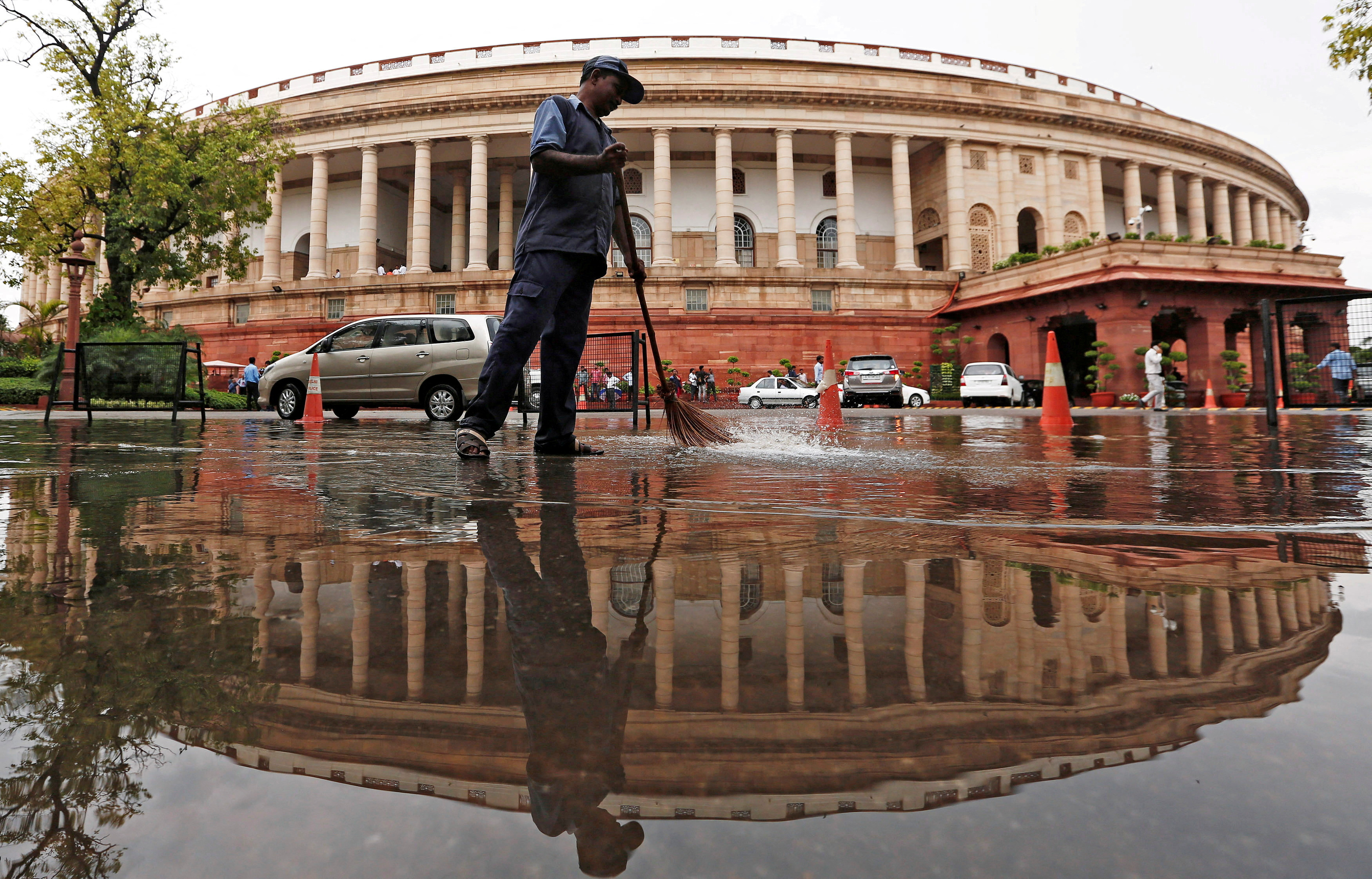 Indian parliament building is reflected in a puddle after the rain as a man sweeps the water in New Delhi