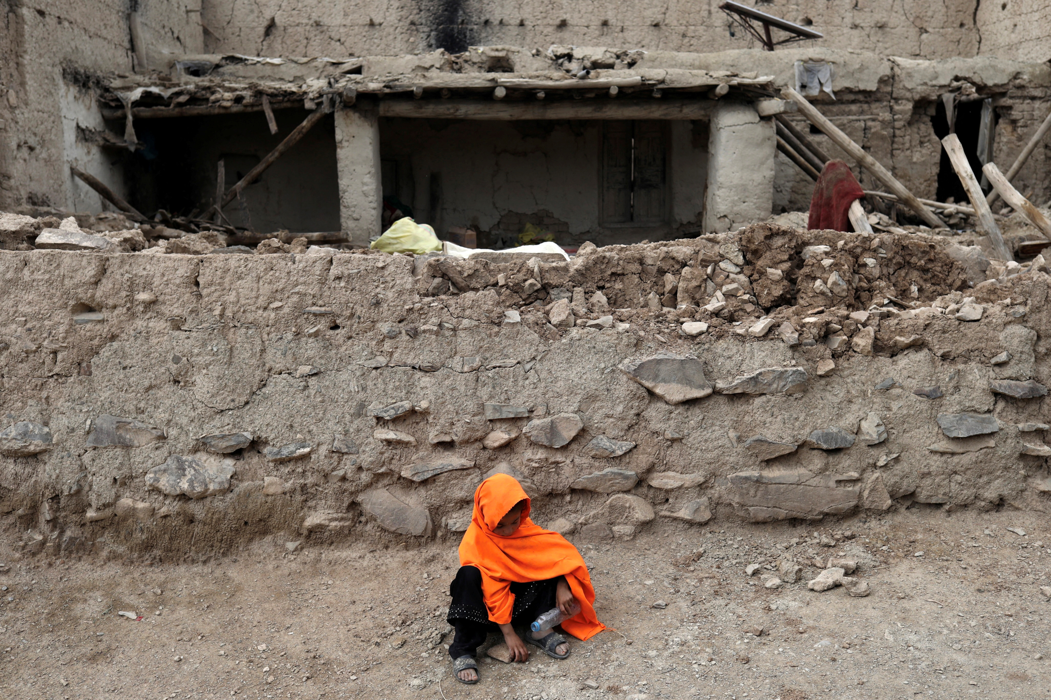 An Afghan girl sits in front of a house that was damaged by an earthquake in Gayan