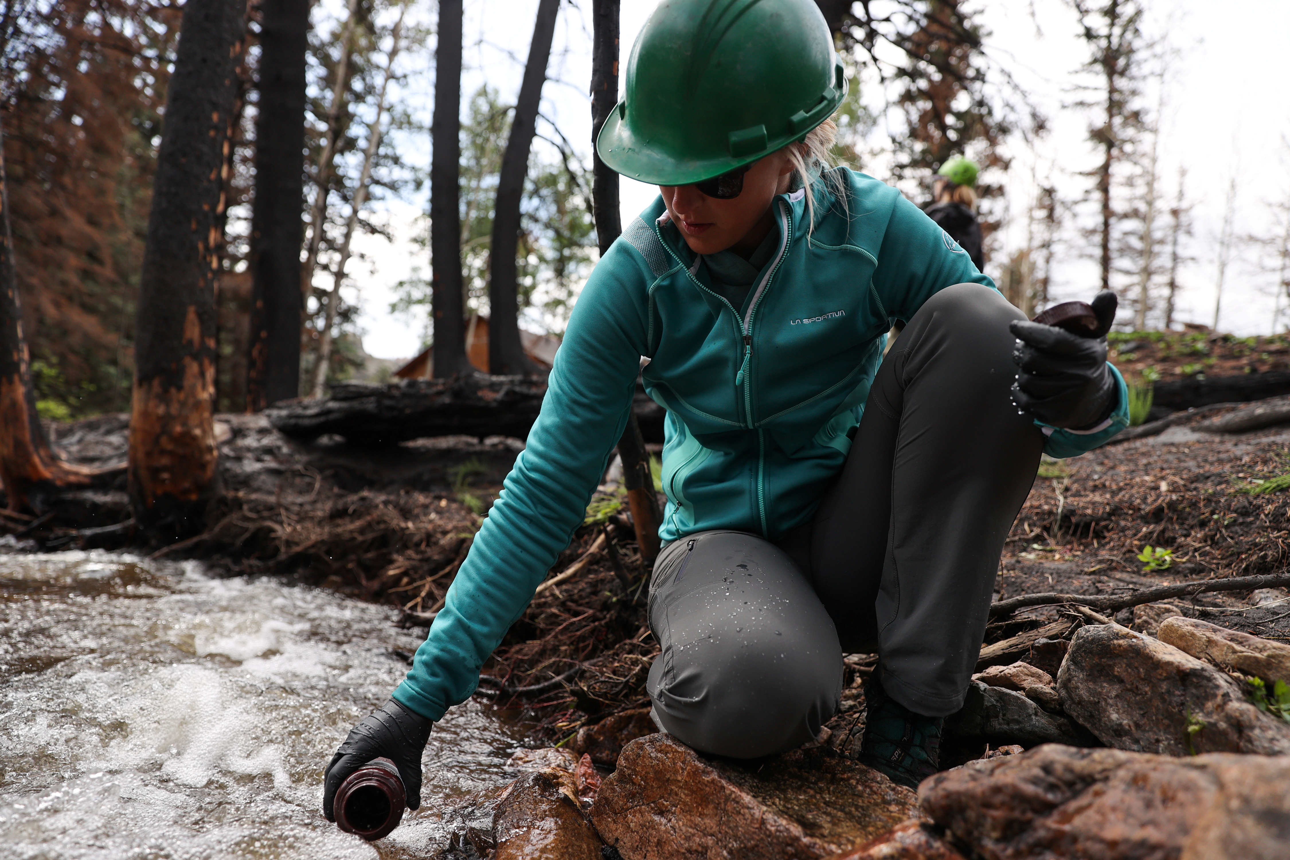 Megan Sears, a field technician with the United States Forest Service, collects a water sample from a tributary to the Poudre River inside the Cameron Peak fire burn scar west of Fort Collins
