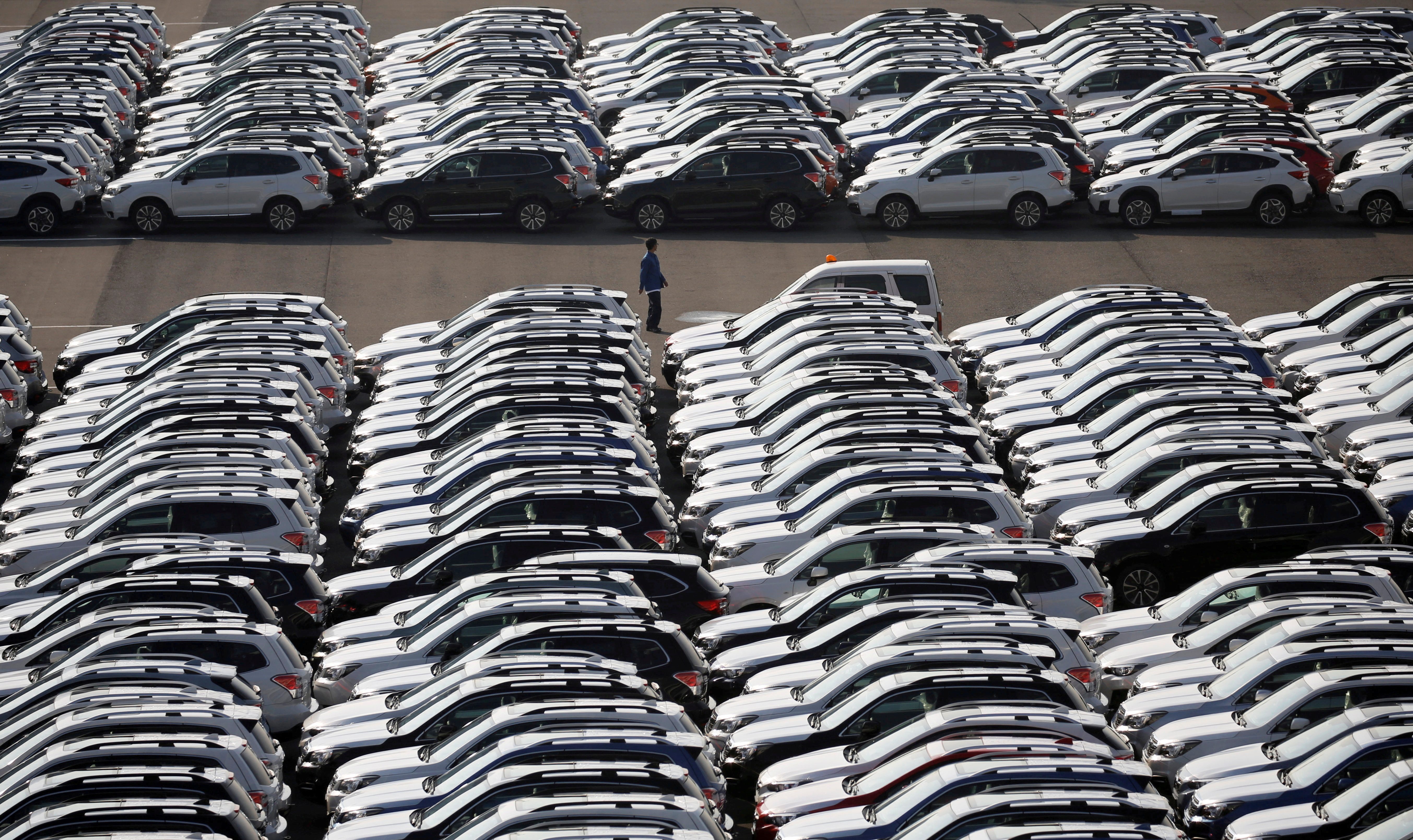 Workers can be seen among newly built cars waiting to be exported at Yokohama port.