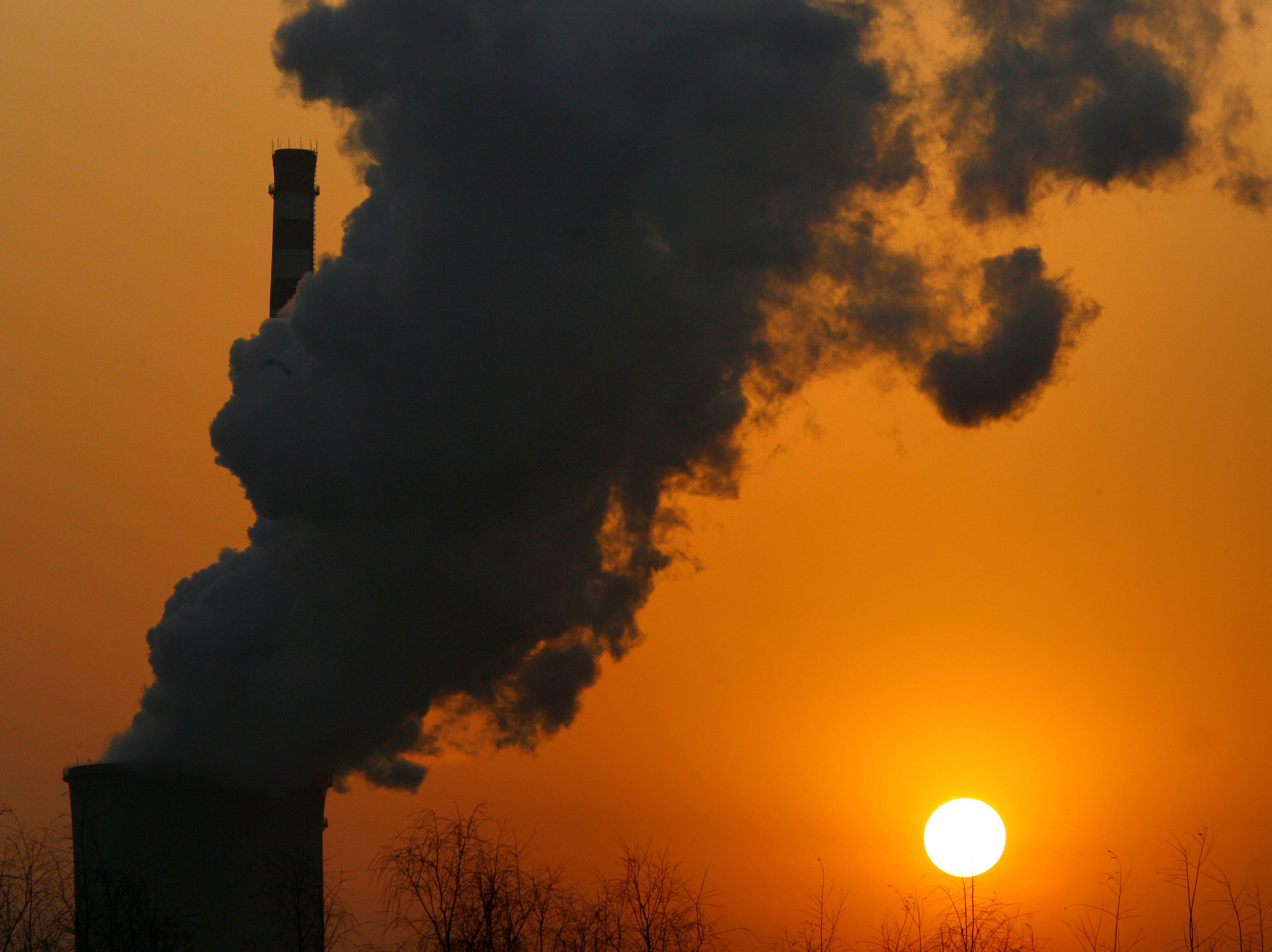 The sun sets next to a smoke stack from a coal-burning power station in Beijing