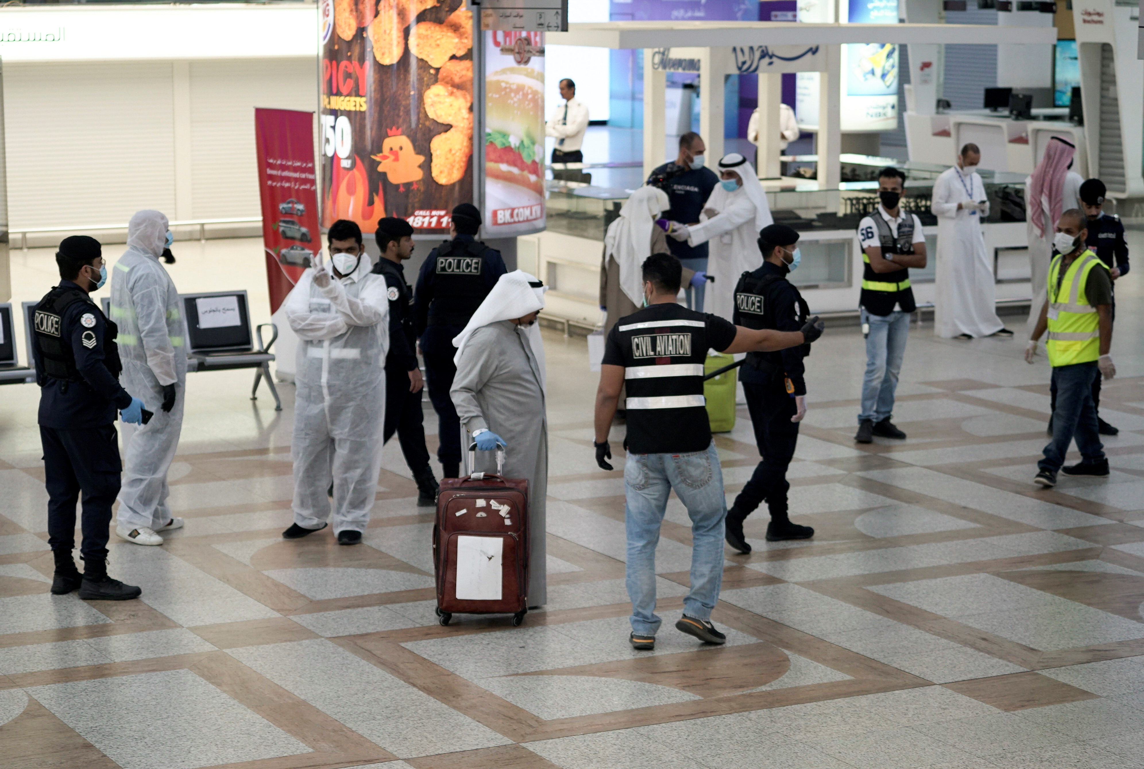 A Kuwaiti passenger holding his luggage walks by the police and civil aviation personnel upon his arrival from Amman at Kuwait Airport, in Kuwait City