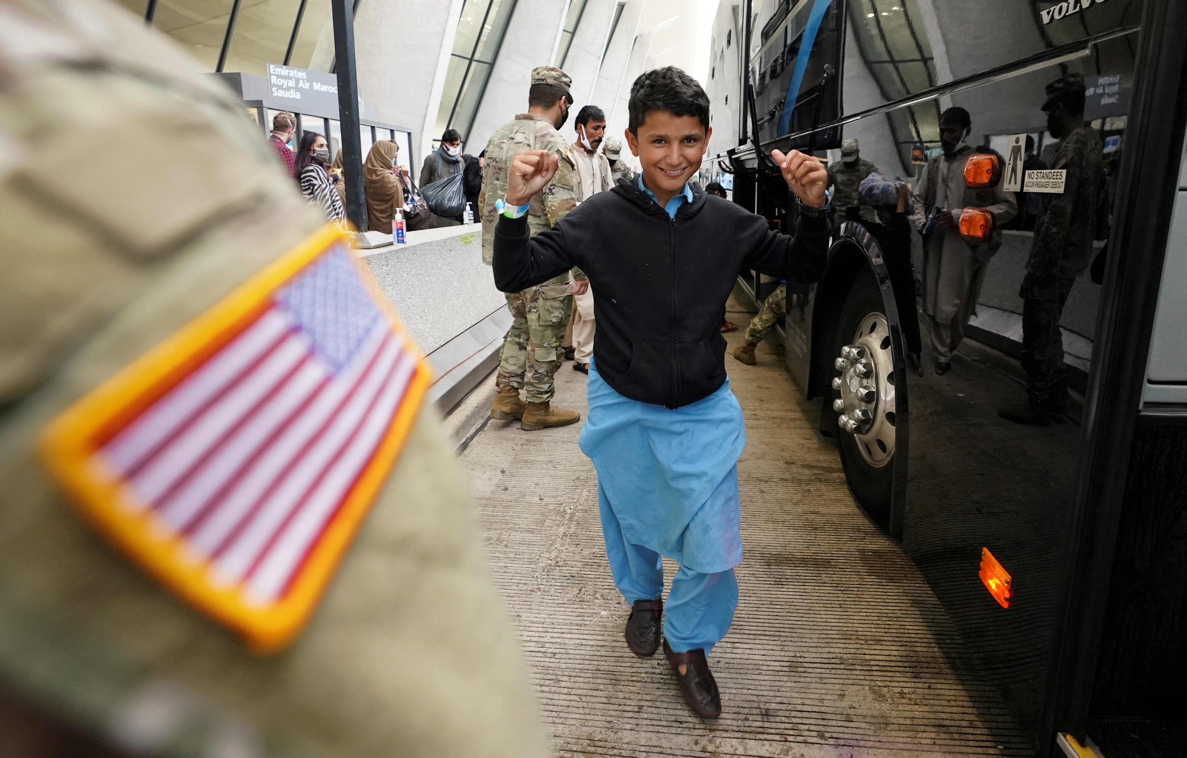 An Afghan boy pumps up his arms as he and other refugees board a bus taking them to a processing center upon their arrival at Dulles International Airport in Dulles, Virginia, U.S.,  September 1, 2021. REUTERS/Kevin Lamarque/File Photo