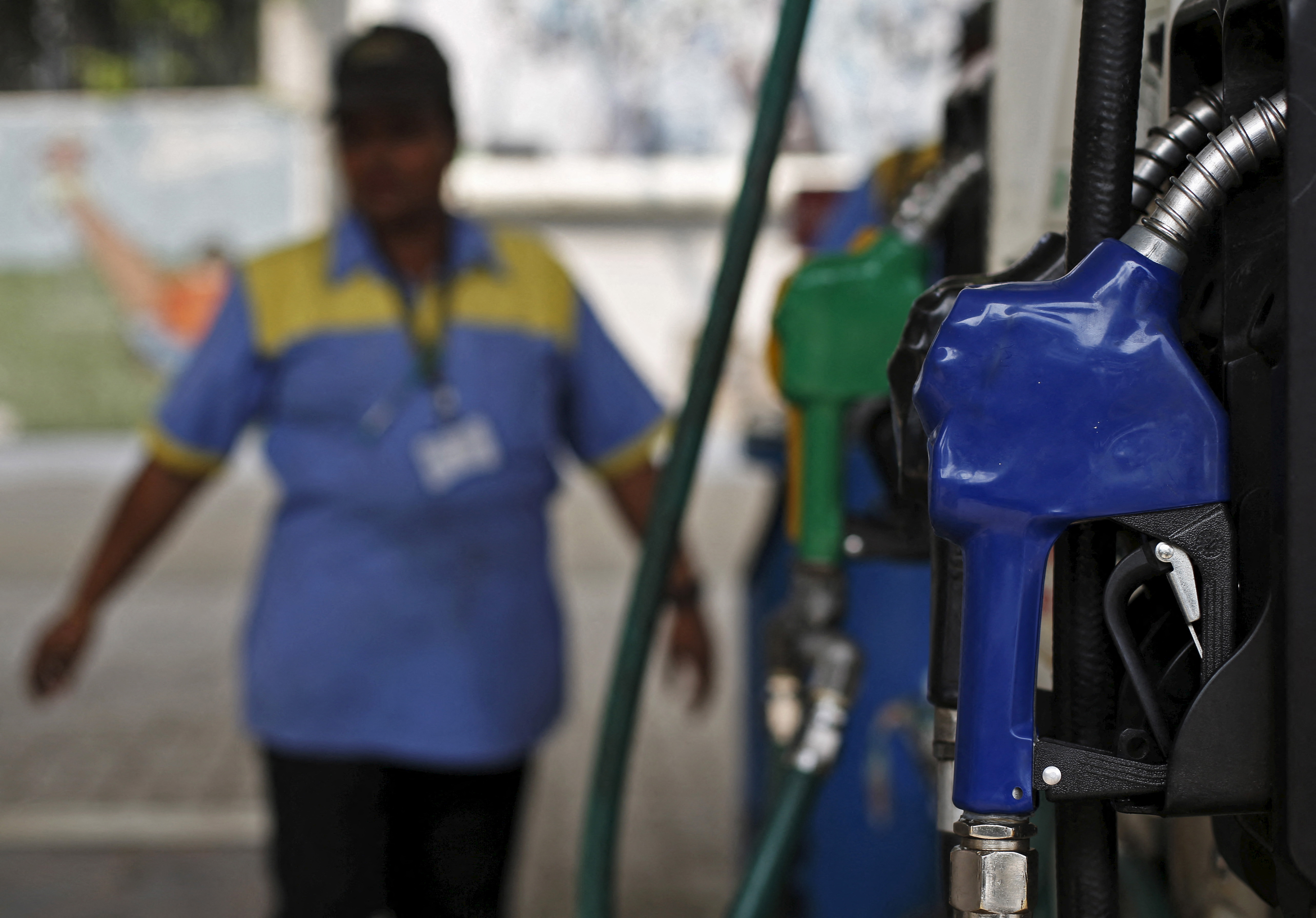 An employee stands next to a fuel pump at a fuel station in New Delhi