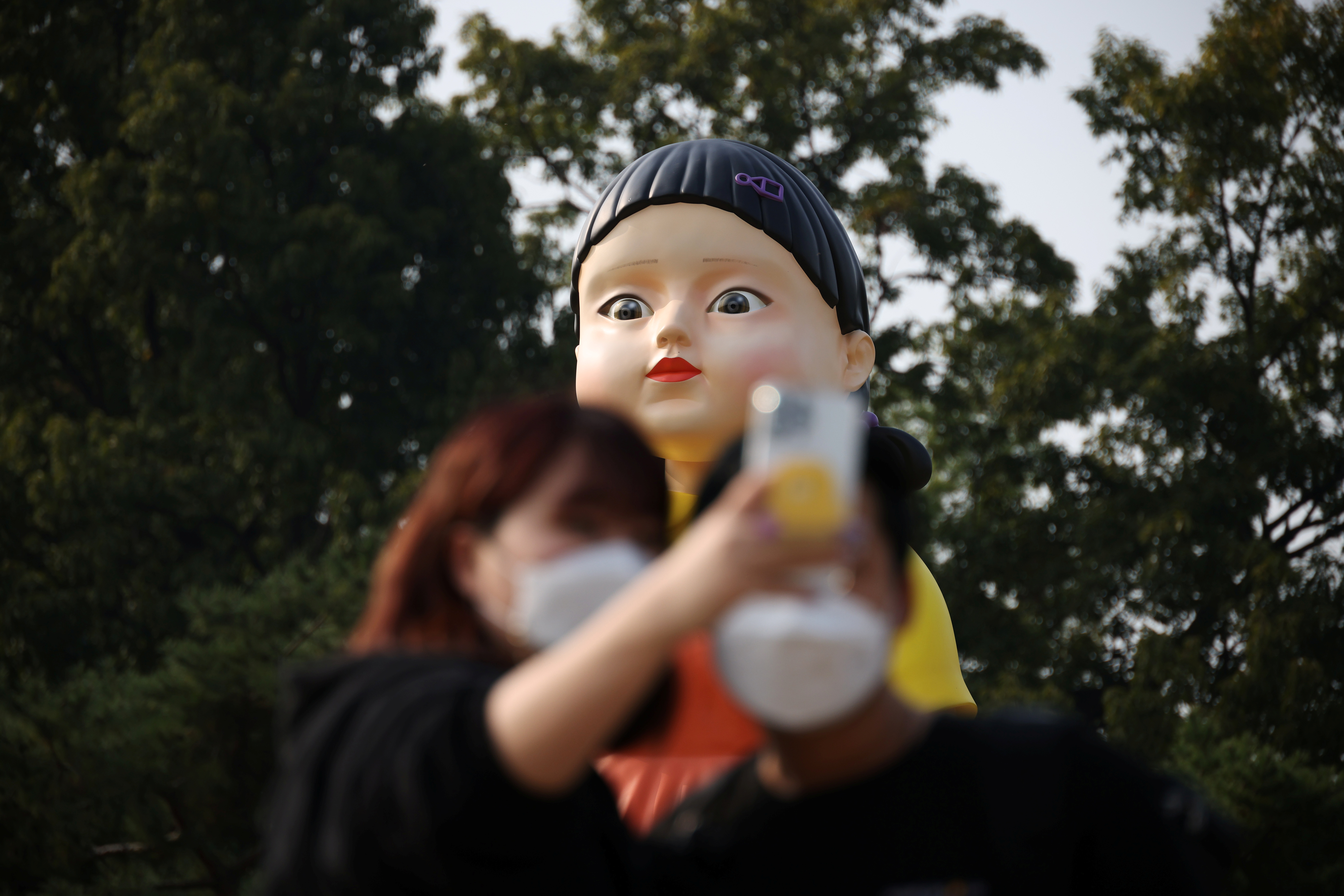 A couple takes a selfie with a giant doll named 'Younghee' from Netflix series 'Squid Game' on display at a park in Seoul