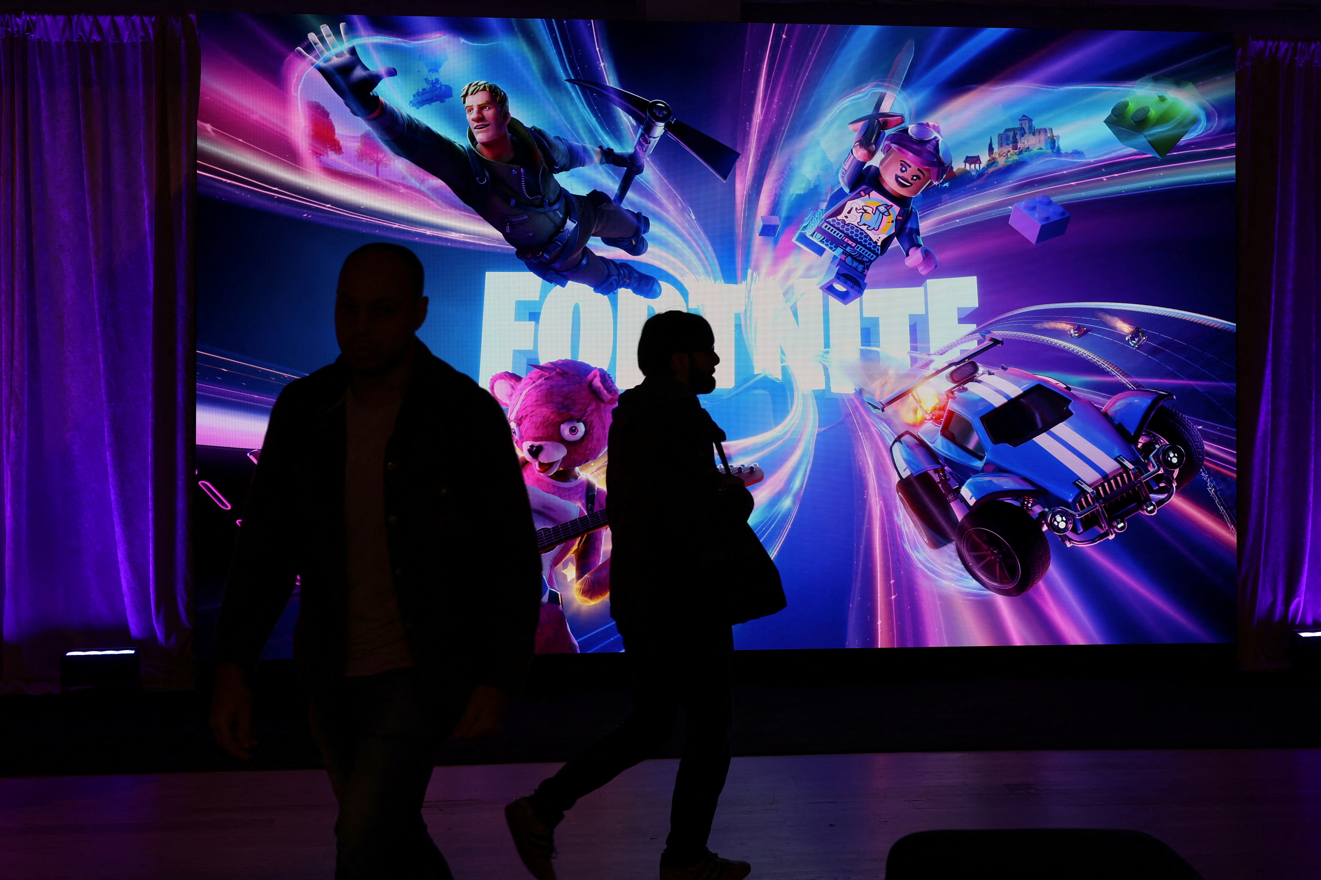 People in silhouette walk by a Fortnite gaming digital monitor during an event in New York City
