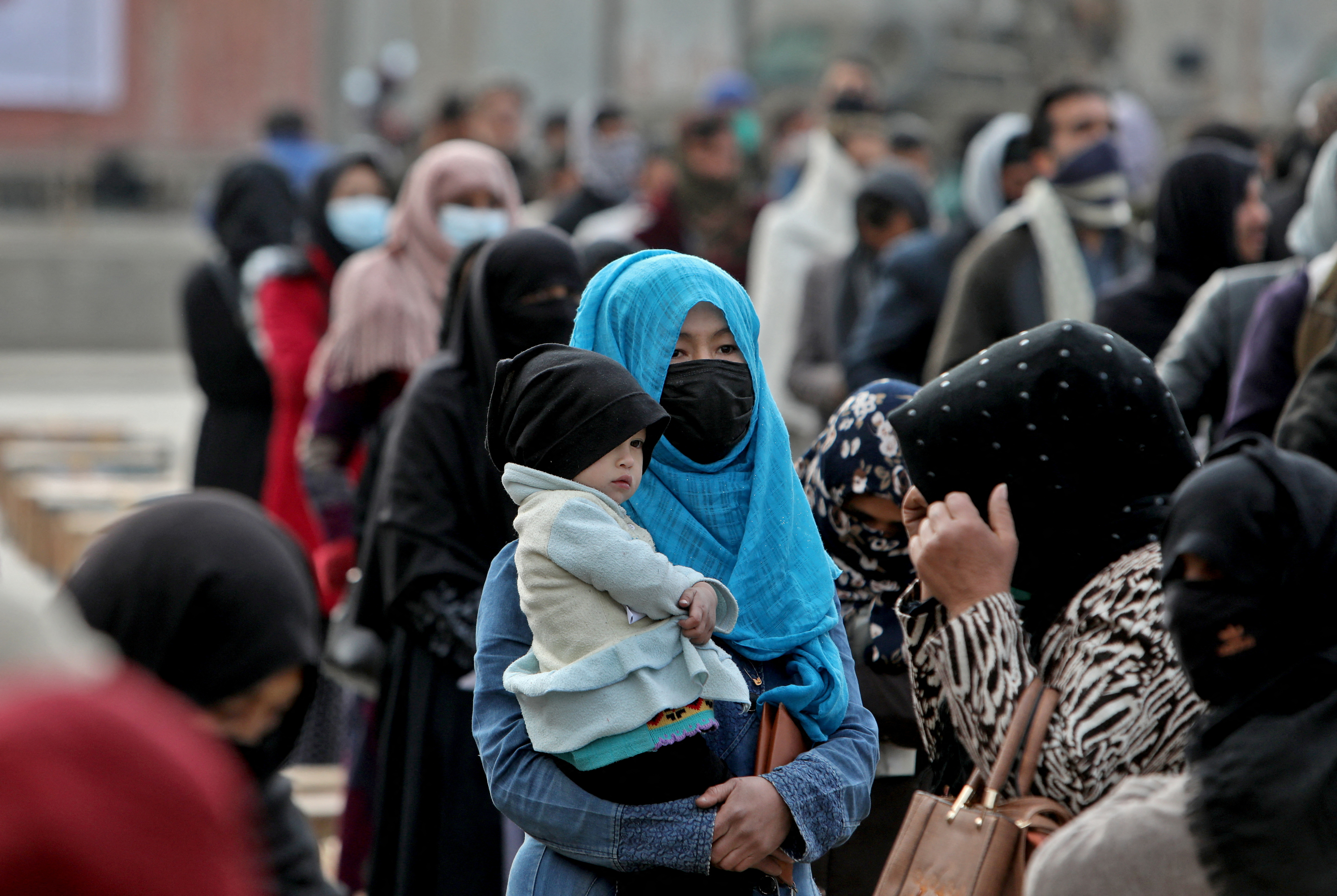 An Afghan woman holds her child as she and others wait to receive package being distributed by a Turkish humanitarian aid group at a distribution centre in Kabul, Afghanistan