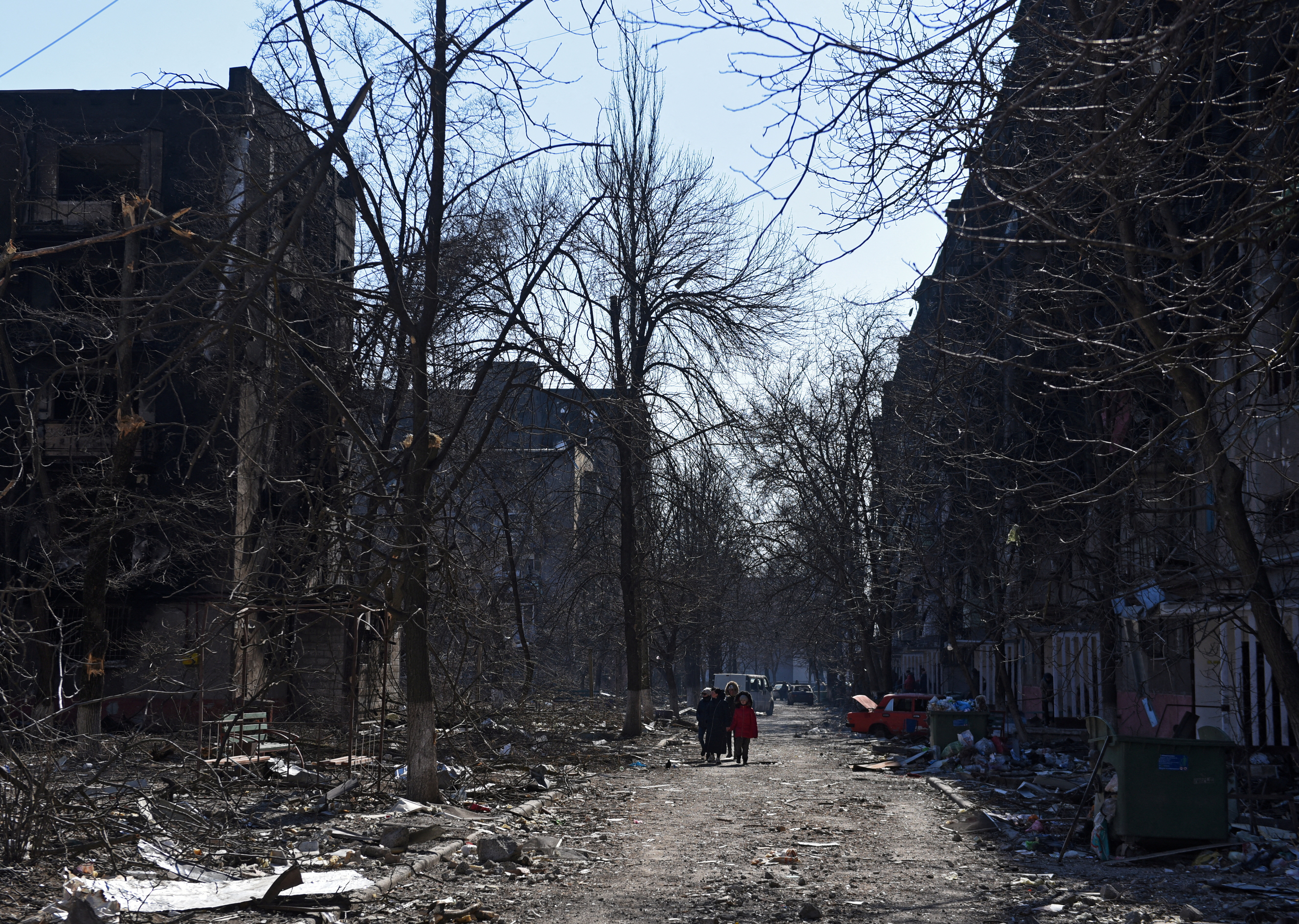 Local residents walk near damaged residential buildings in the besieged city of Mariupol