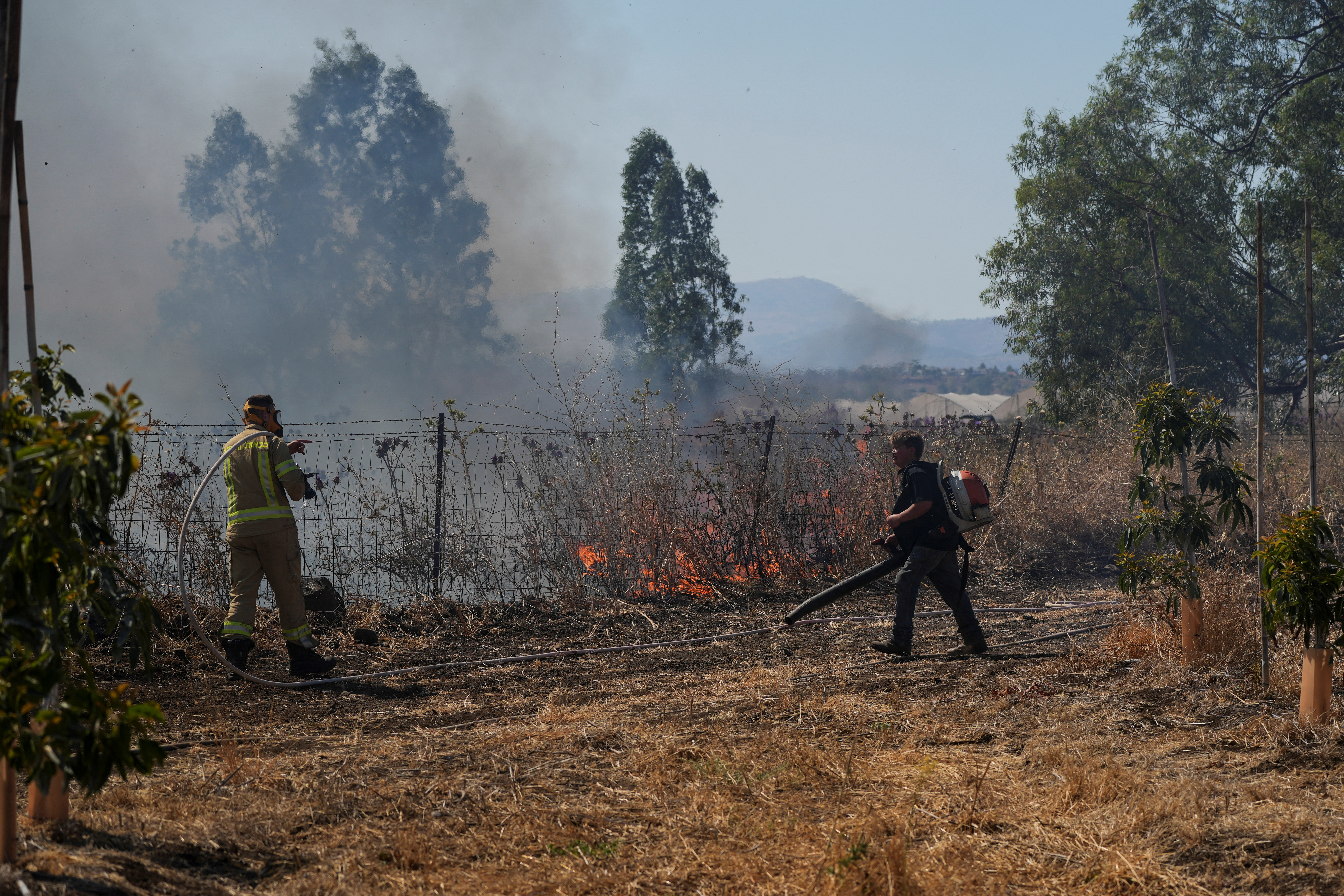 Israeli fire-fighter and another man work to take control over fire following rocket attacks from Lebanon