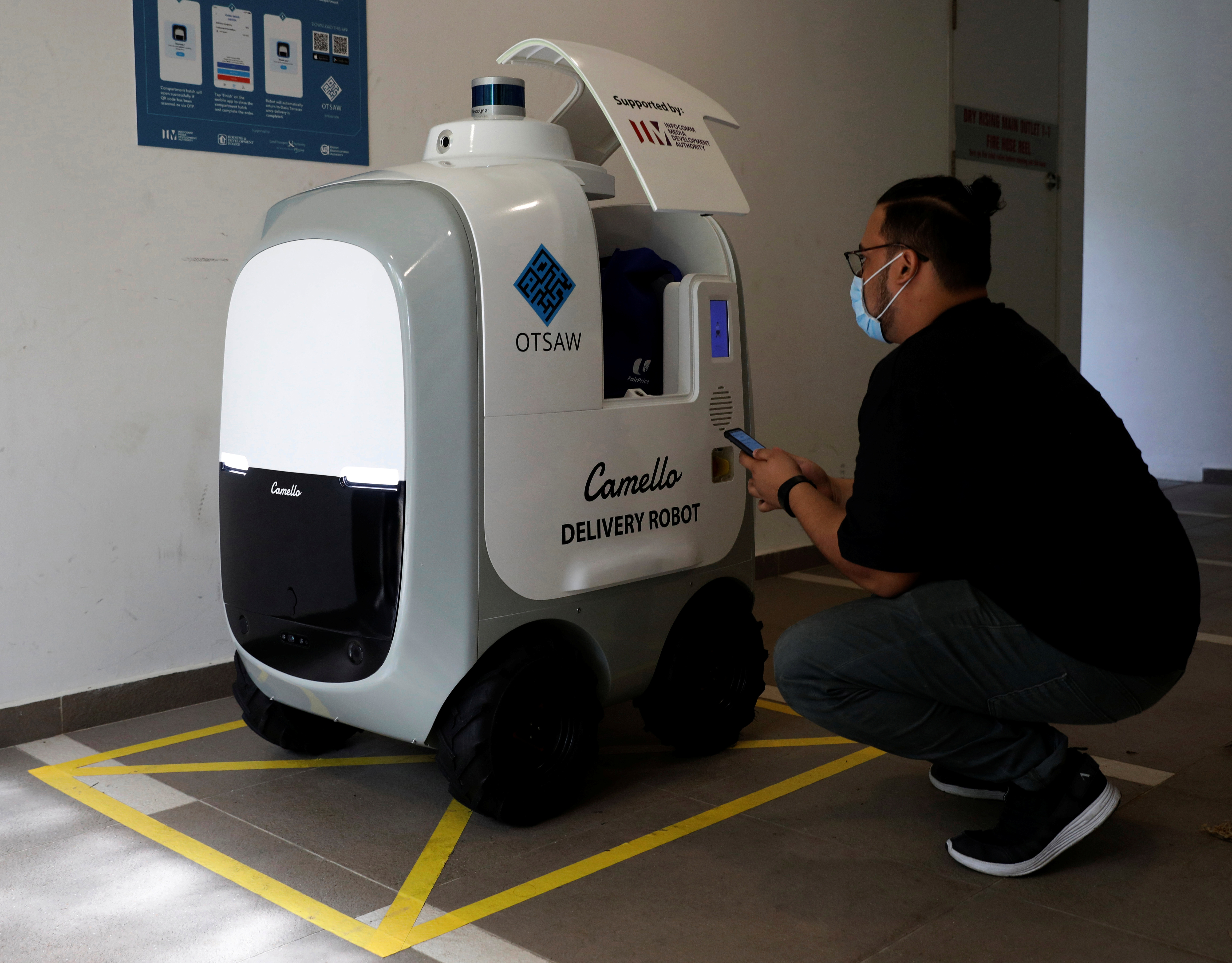 A customer collects his groceries from Camello, an autonomous grocery delivery robot, in Singapore