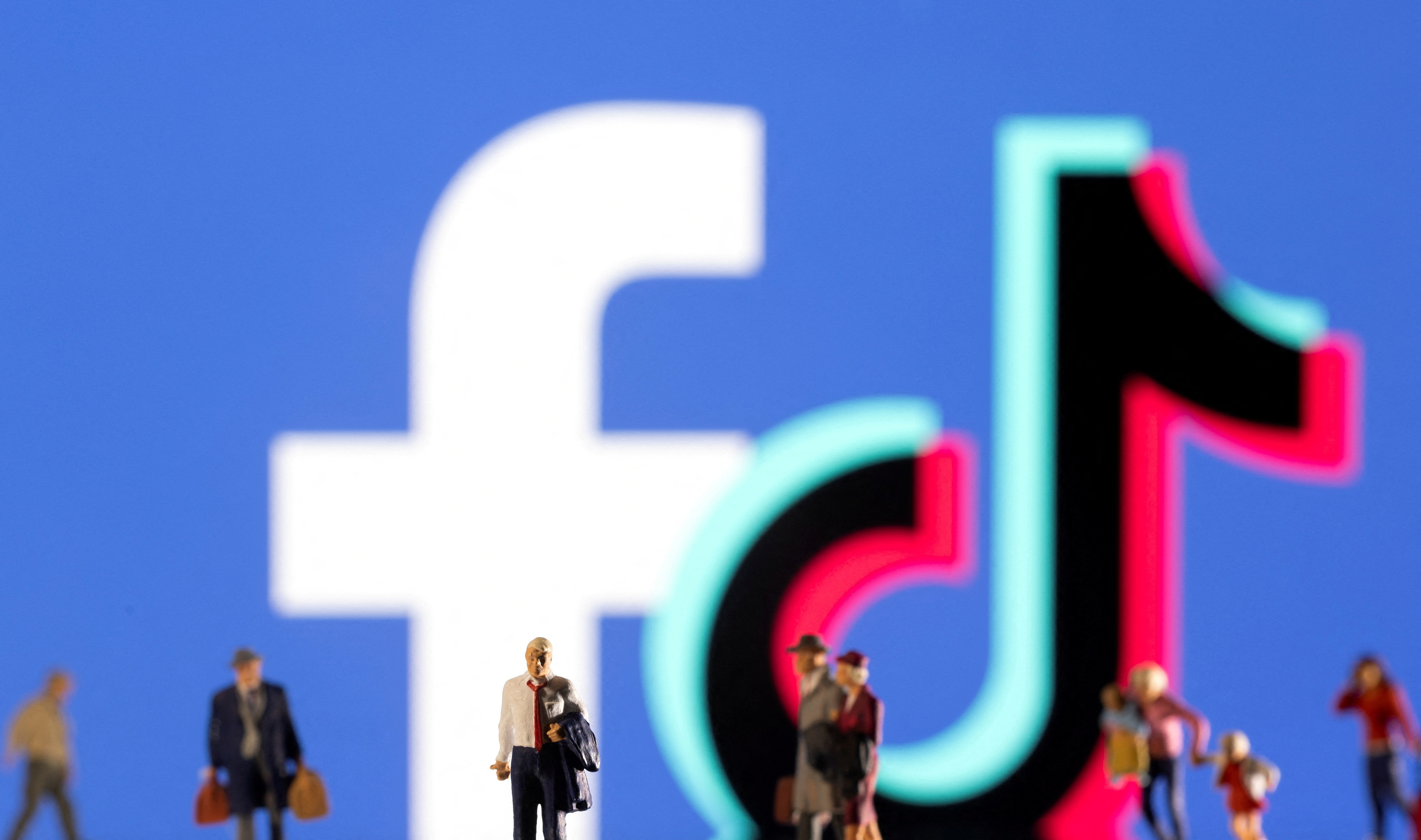 Illustration shows small figurines and displayed Tik Tok and Facebook logos