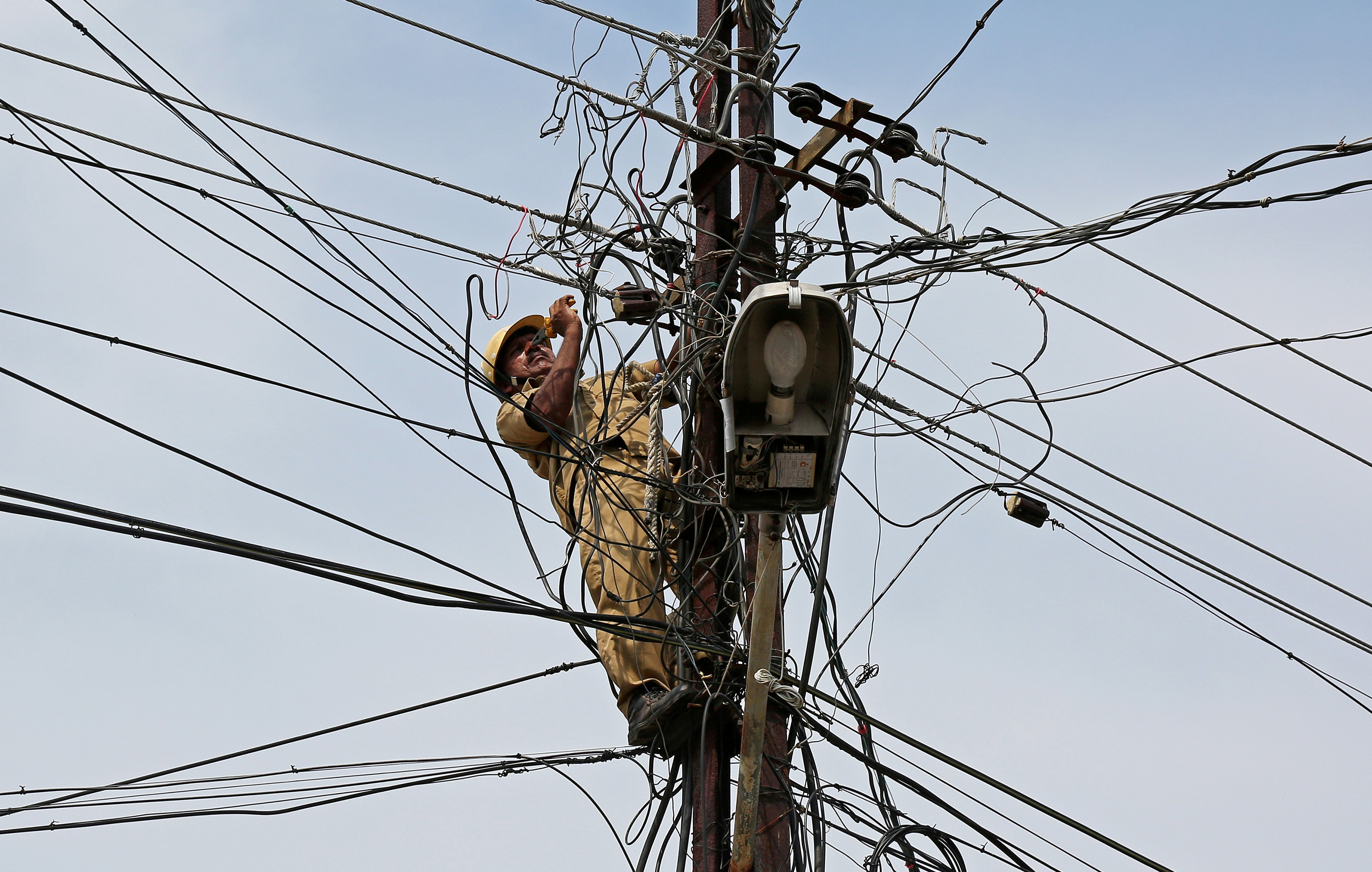 A worker repairs power lines on a pole in Kochi