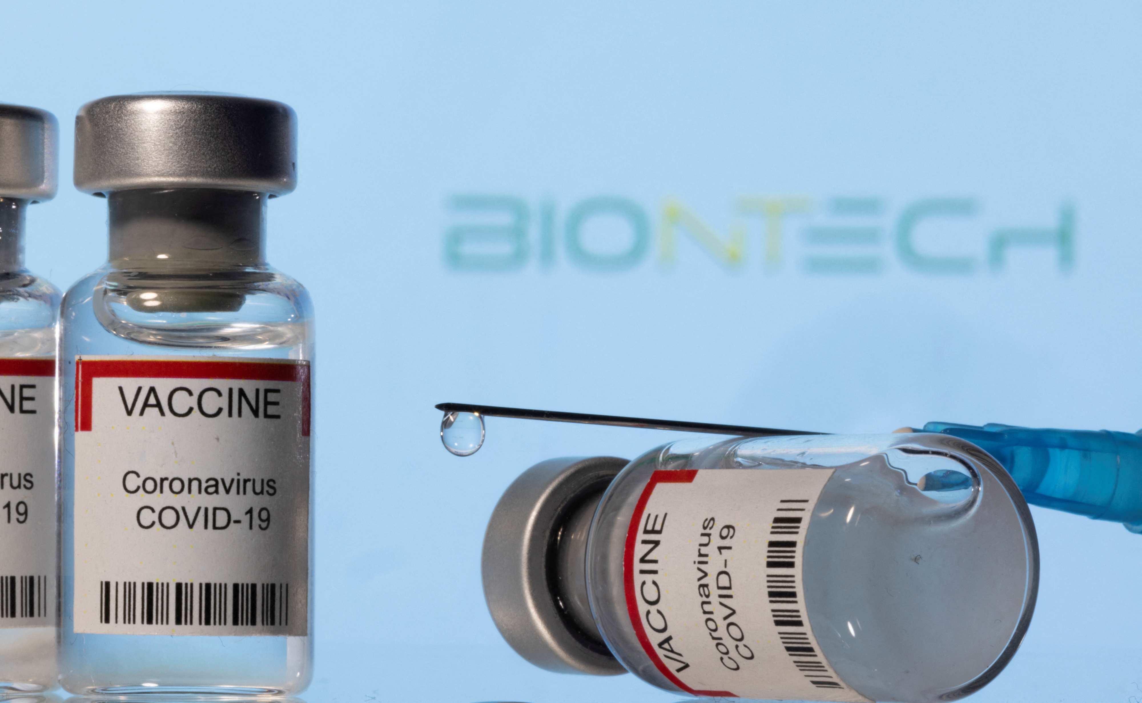 Illustration shows vials labelled "VACCINE Coronavirus COVID-19" and a syringe in front of a displayed Biontech logo