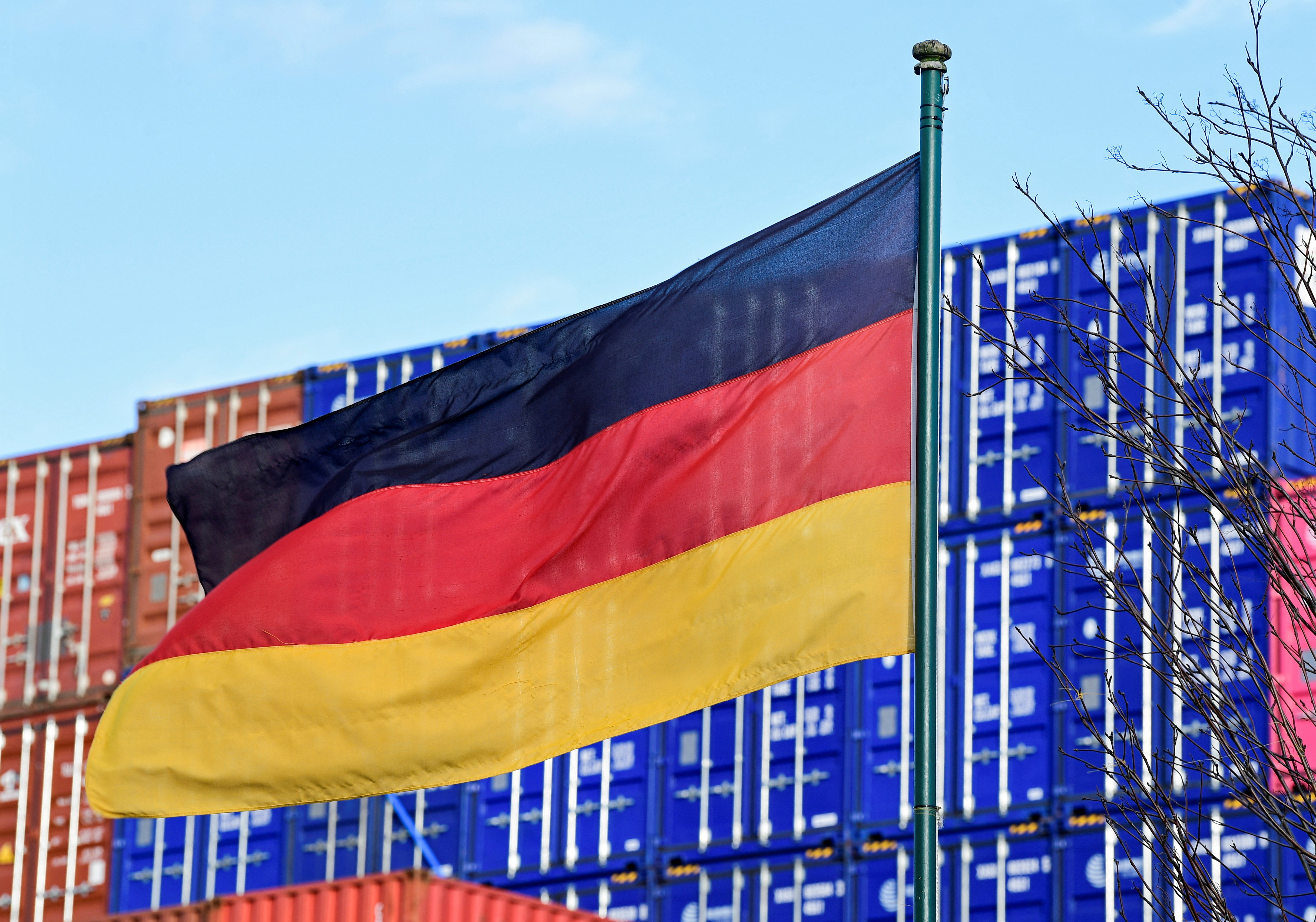 A German flag blows in the wind in front of a stack of containers at the harbour in Hamburg