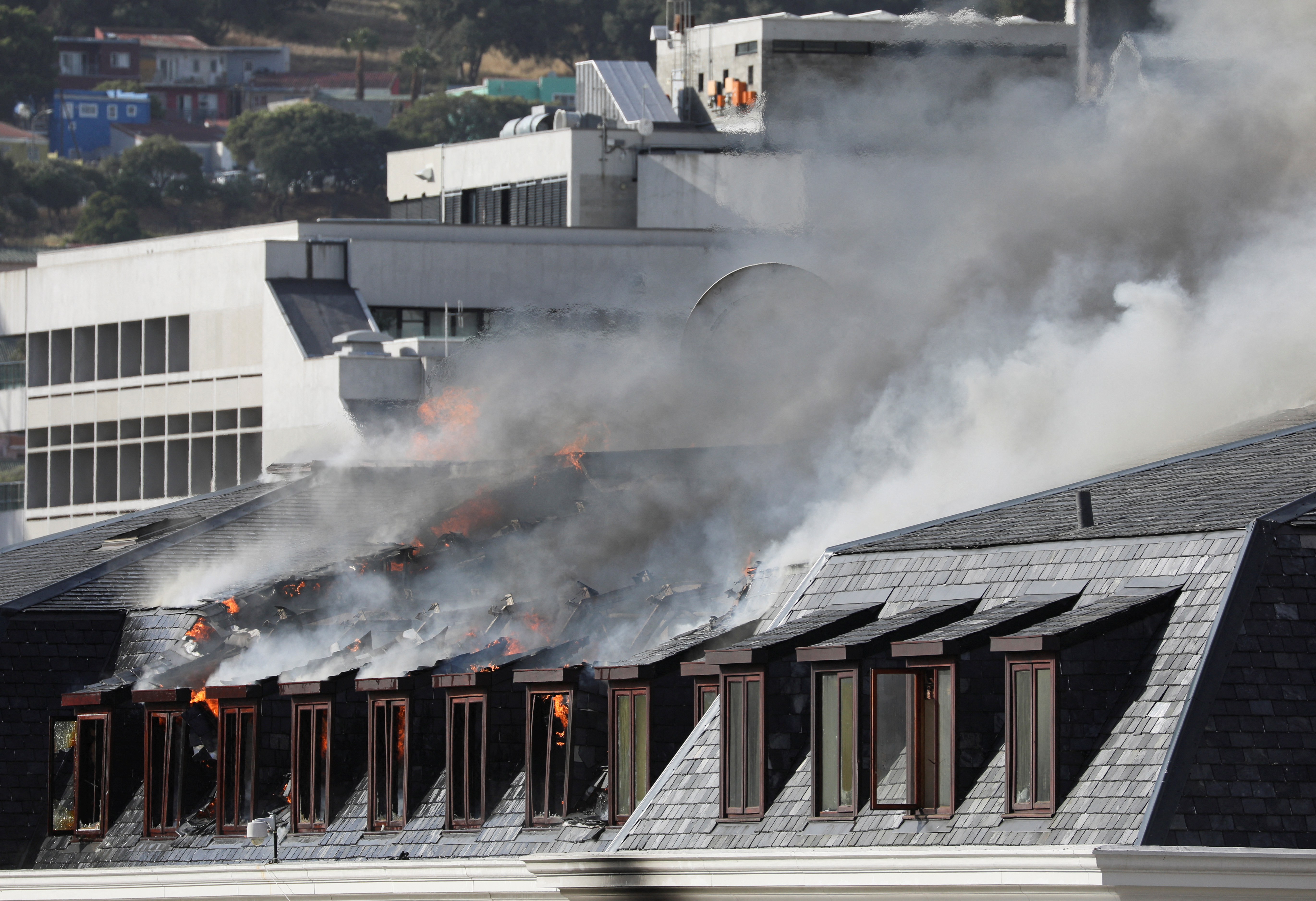 Flames and smoke rise over a roof as the fire at the parliament flared up again, in Cape Town, South Africa, January 3, 2022. REUTERS/Sumaya Hisham