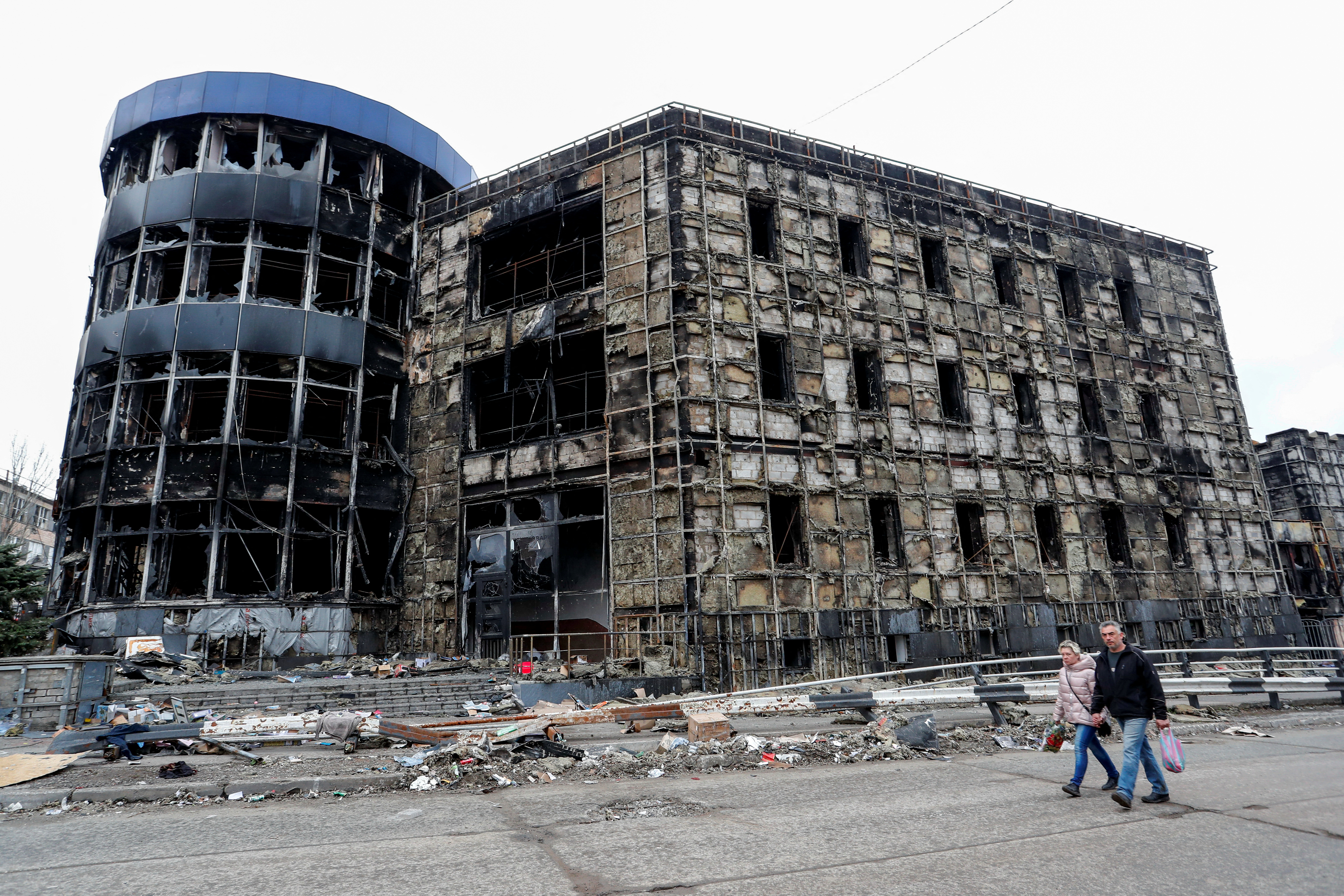 People walk past a destroyed building in Mariupol