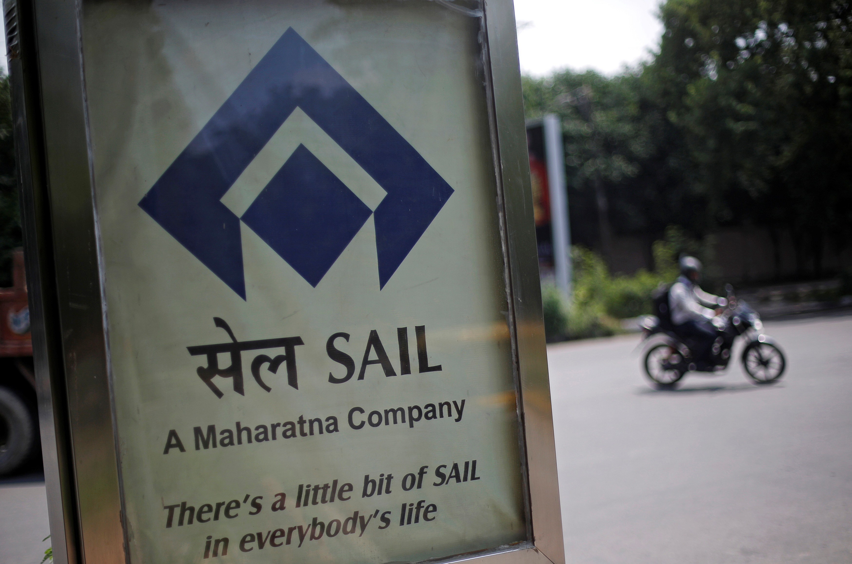 A motorcyclist rides past an advertisement of SAIL at a street in New Delhi