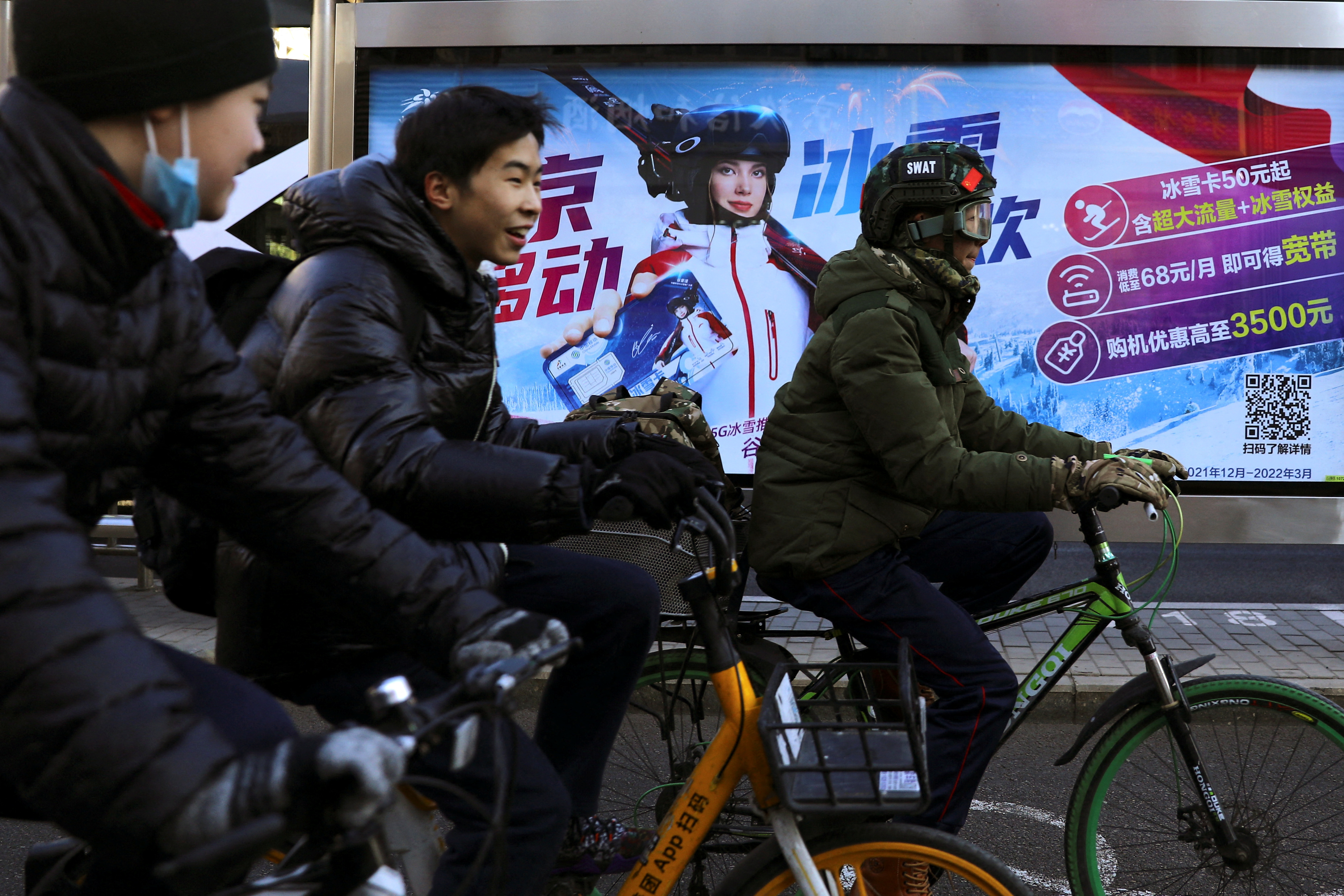 People ride bicycles past an advertisement with an image of Eileen Gu, at a bus stop in Beijing