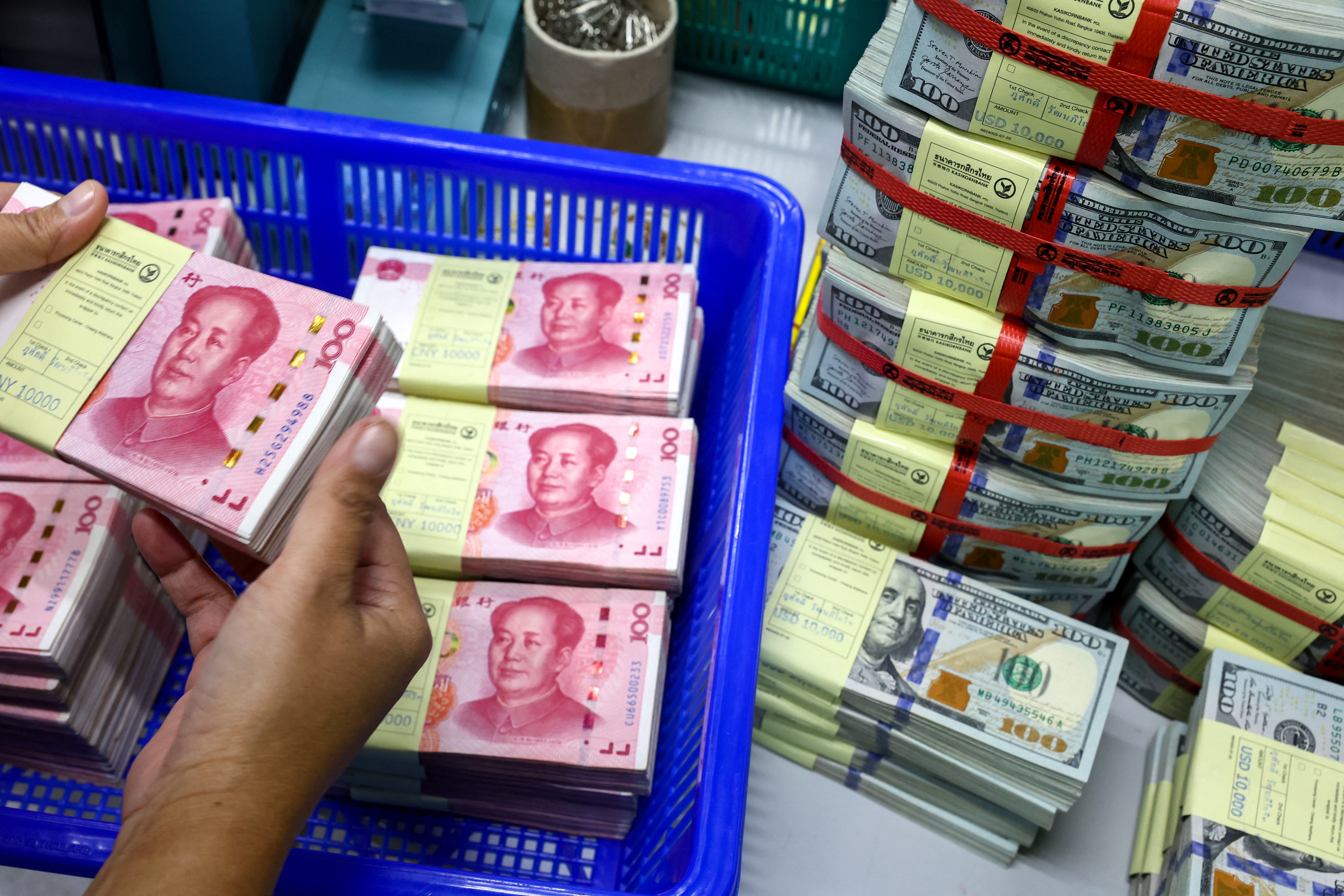 A bank employee count China’s renminbi (RMB) or yuan notes next to U.S. dollar notes at a Kasikornbank in Bangkok