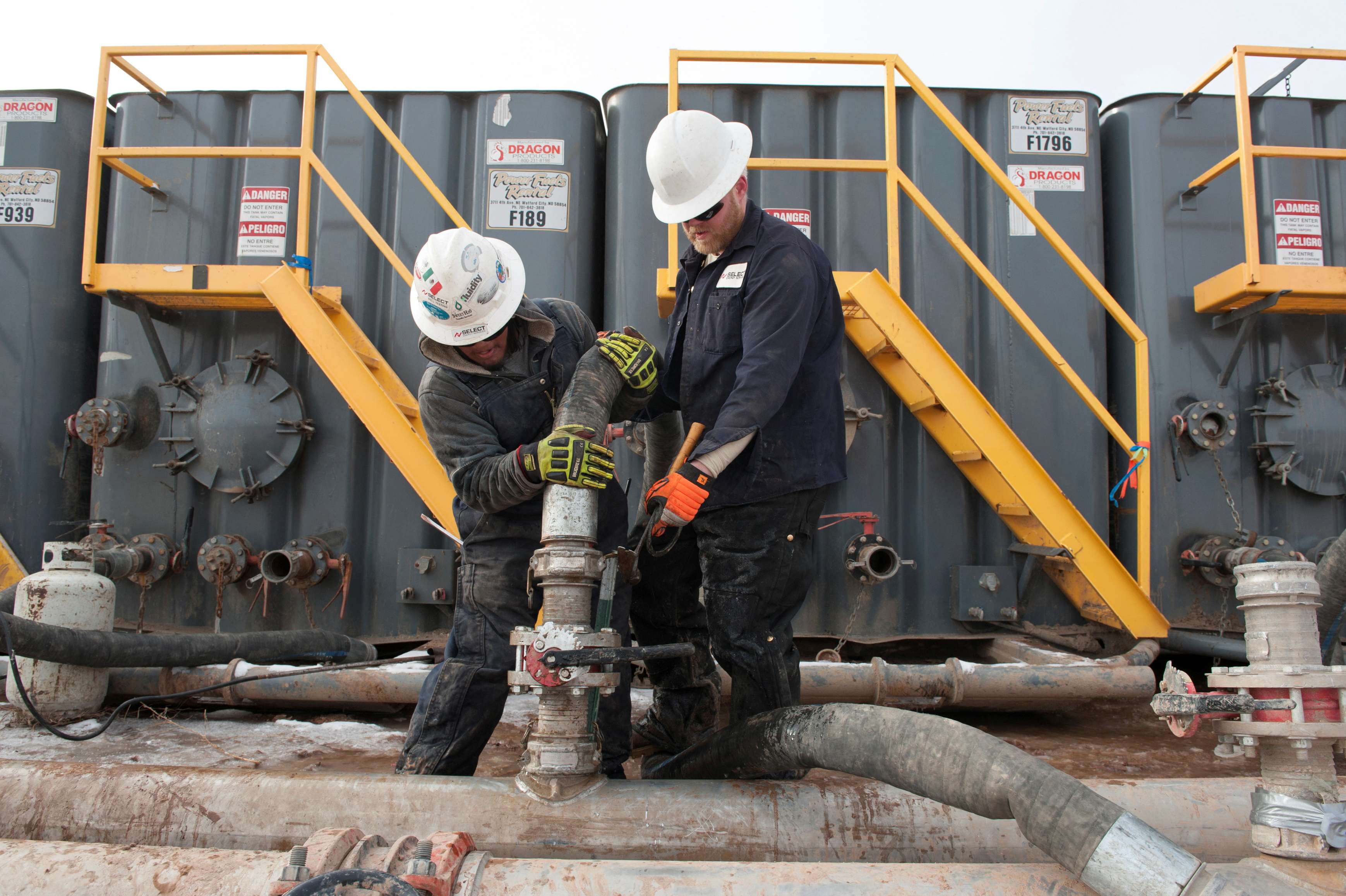 Workers connect hoses between a pipeline and water tanks at a Hess fracking site near Williston