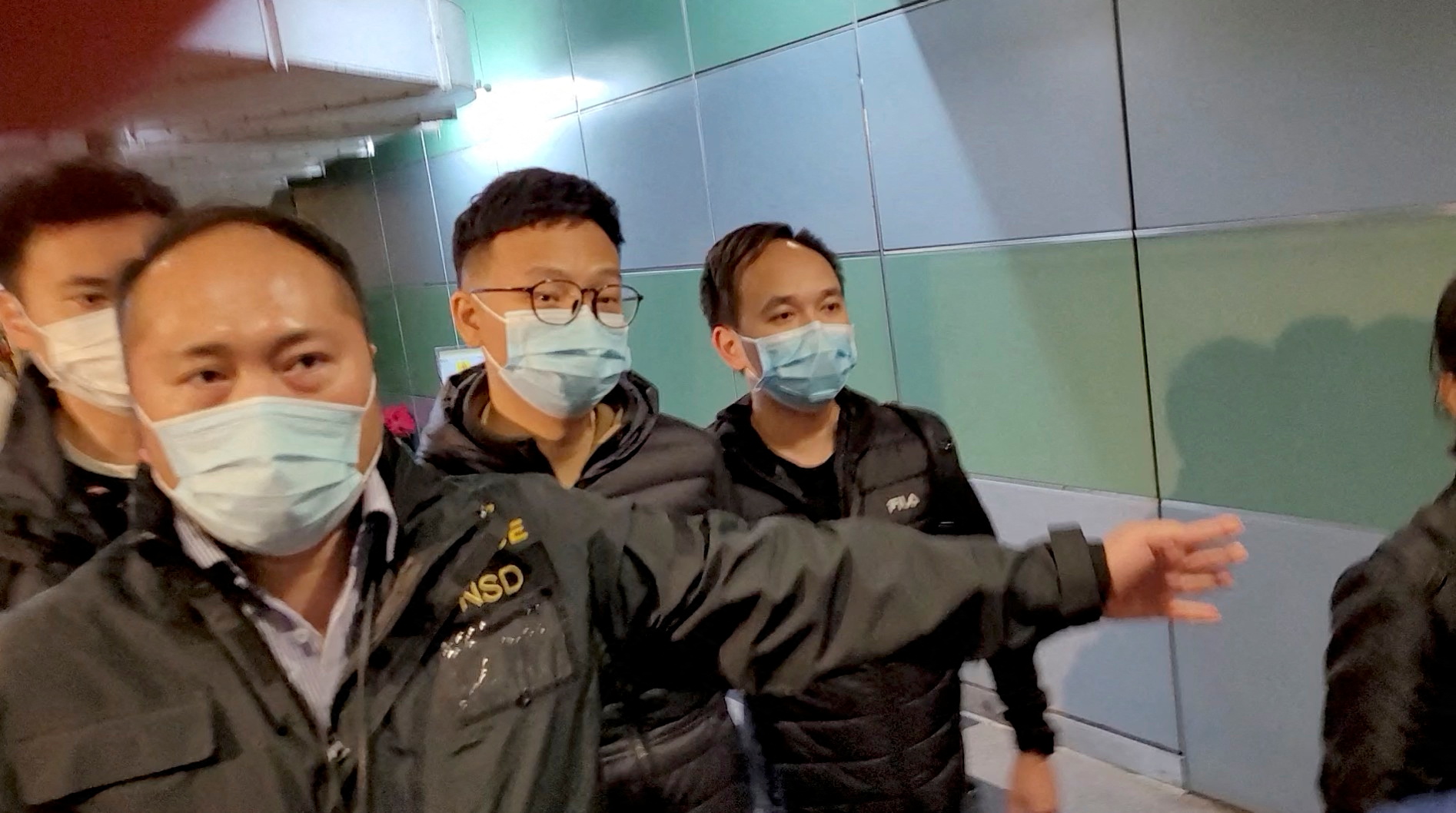Police officers escort Stand News editor Patrick Lam through a building hallway in Hongkong