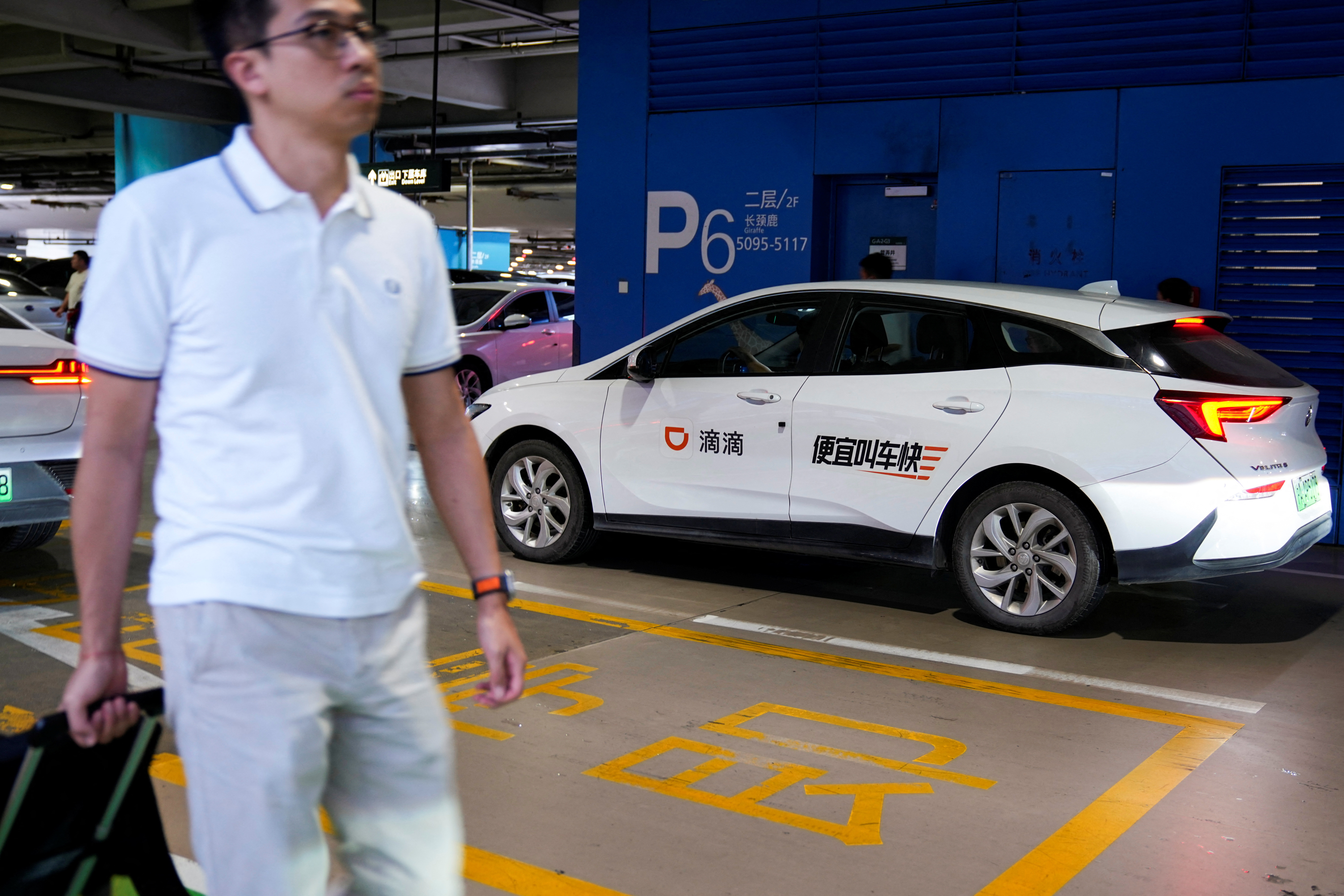 A man passes by a car of Chinese ride-hailing service Didi at the Shanghai Hongqiao International Airport in Shanghai