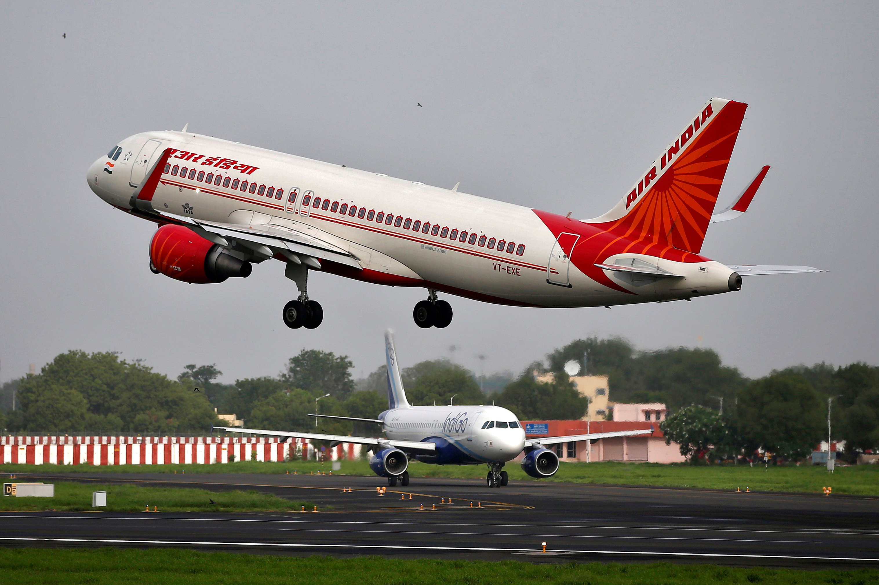 An Air India Airbus A320 aircraft takes off as an IndiGo Airlines aircraft waits for clearance at the Sardar Vallabhbhai Patel International Airport in Ahmedabad