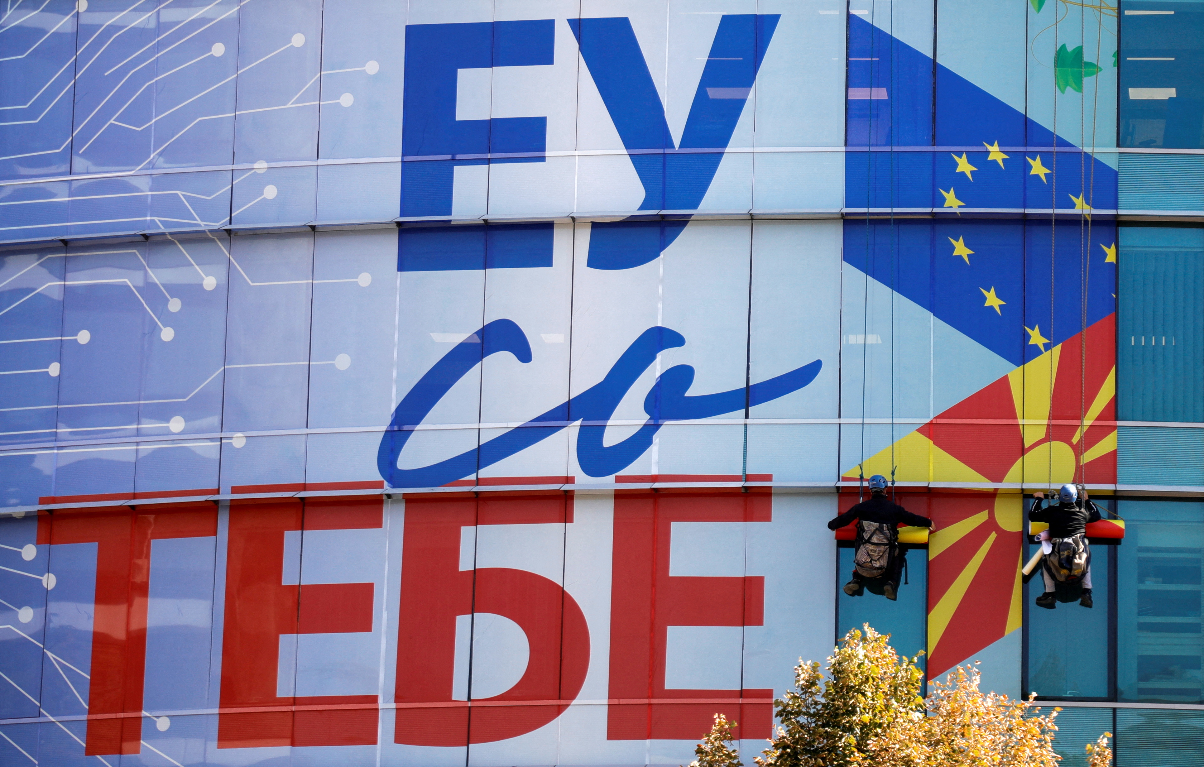 Workers add a new decorative poster saying 'EU with you' on the windows of the offices of the European Union in Skopje