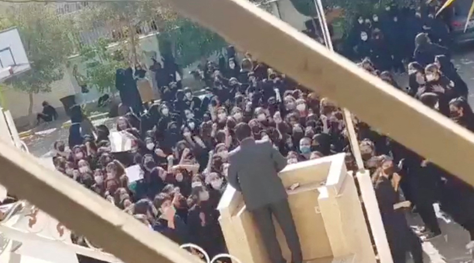 Female protesters react and chant towards a man standing at a podium in Shiraz