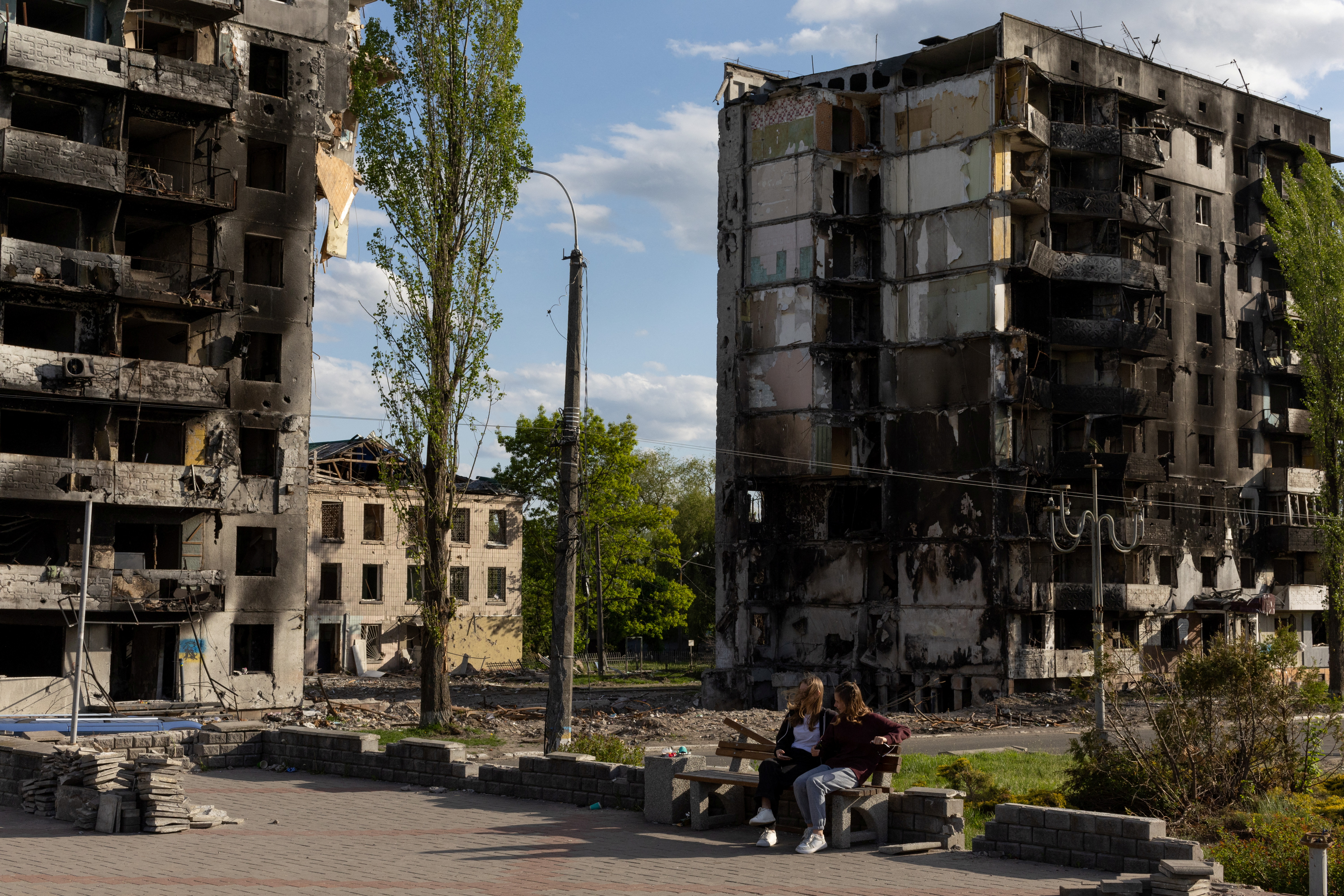 Two girls sit in a a public square in front of destroyed buildings amid Russia's invasion of Ukraine, in Borodyanka