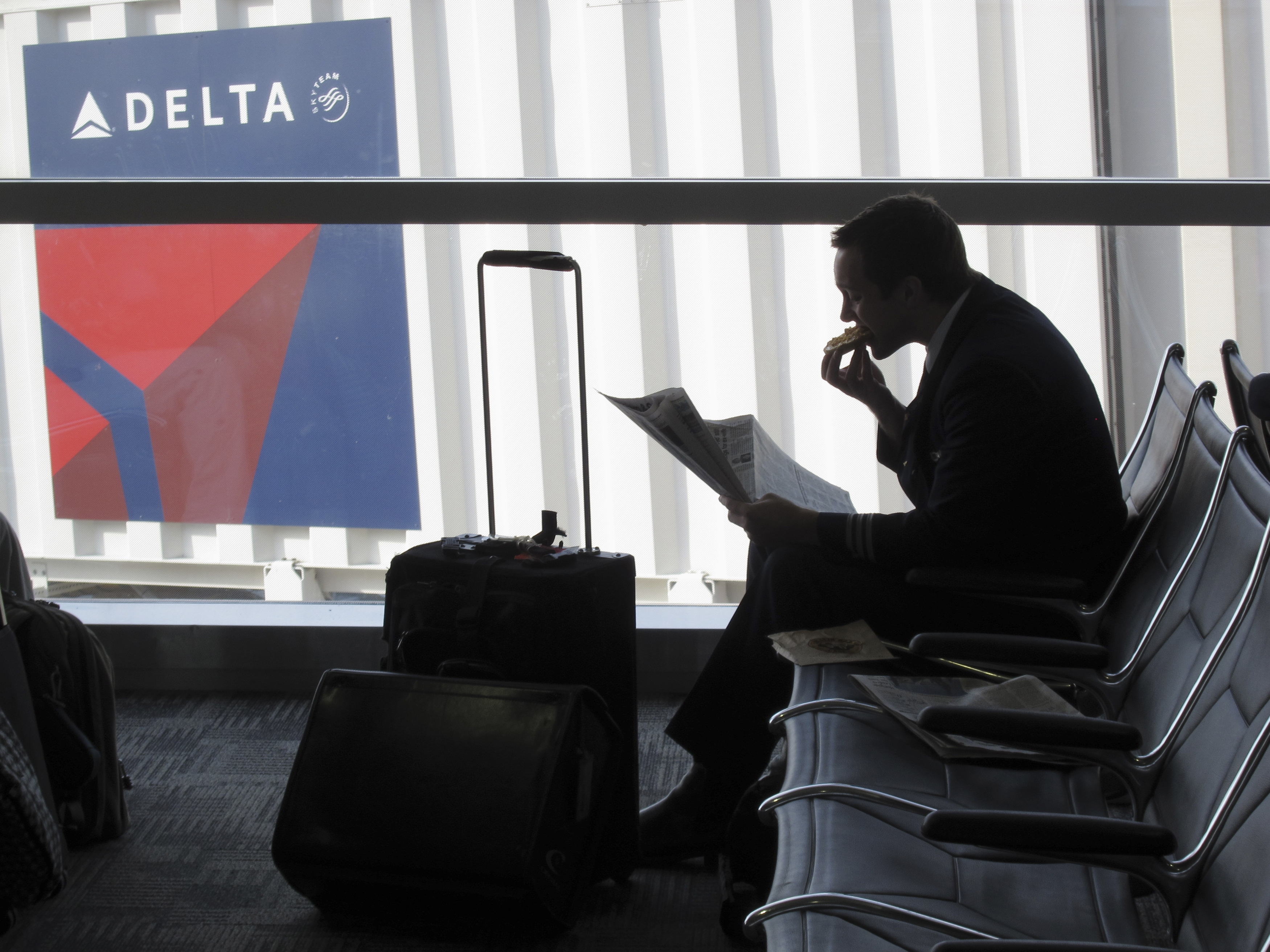 Passenger waits for his flight near a Delta Air Lines logo at Detriot Airport