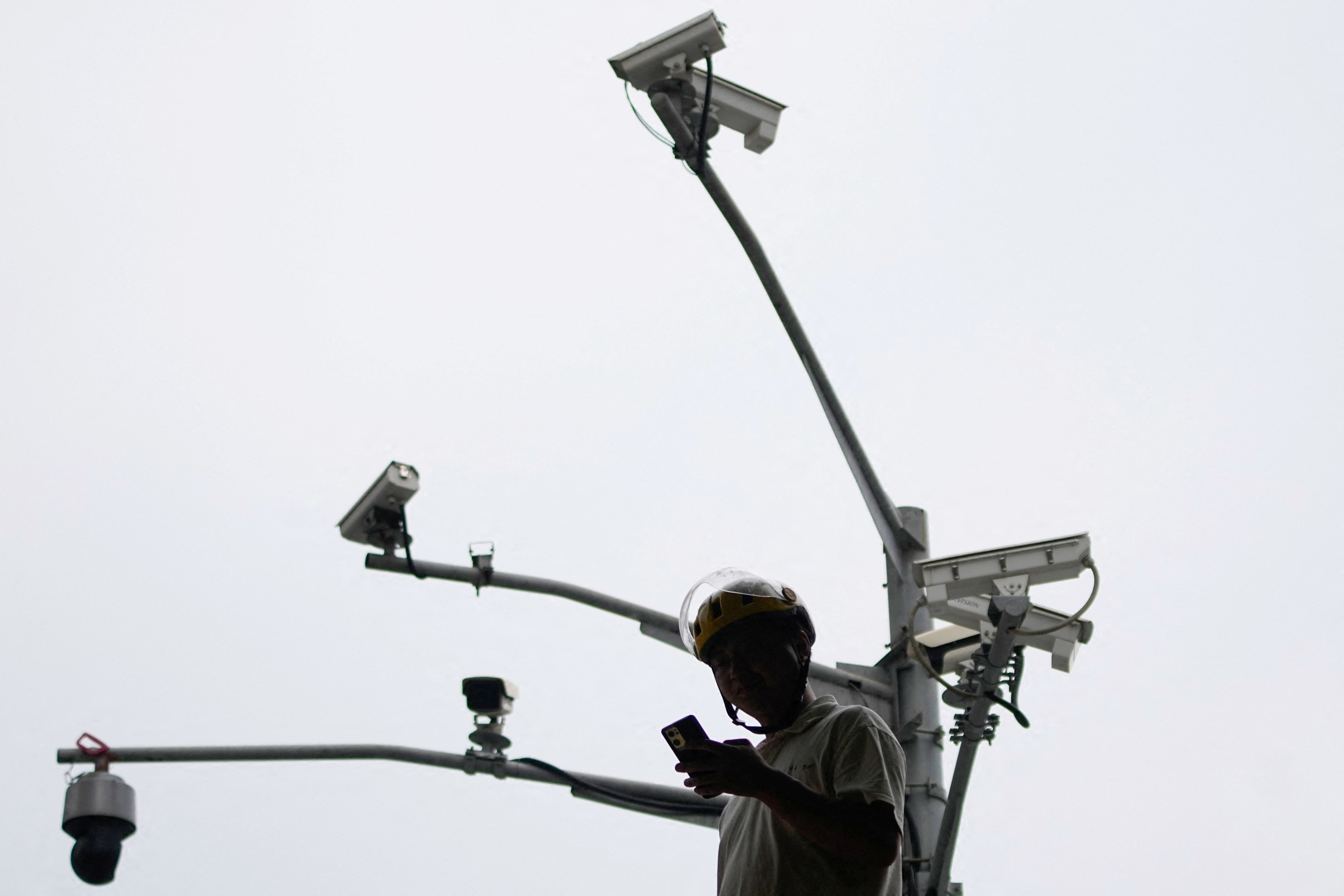 A man looks at a phone under surveillance cameras on a street, in Shanghai