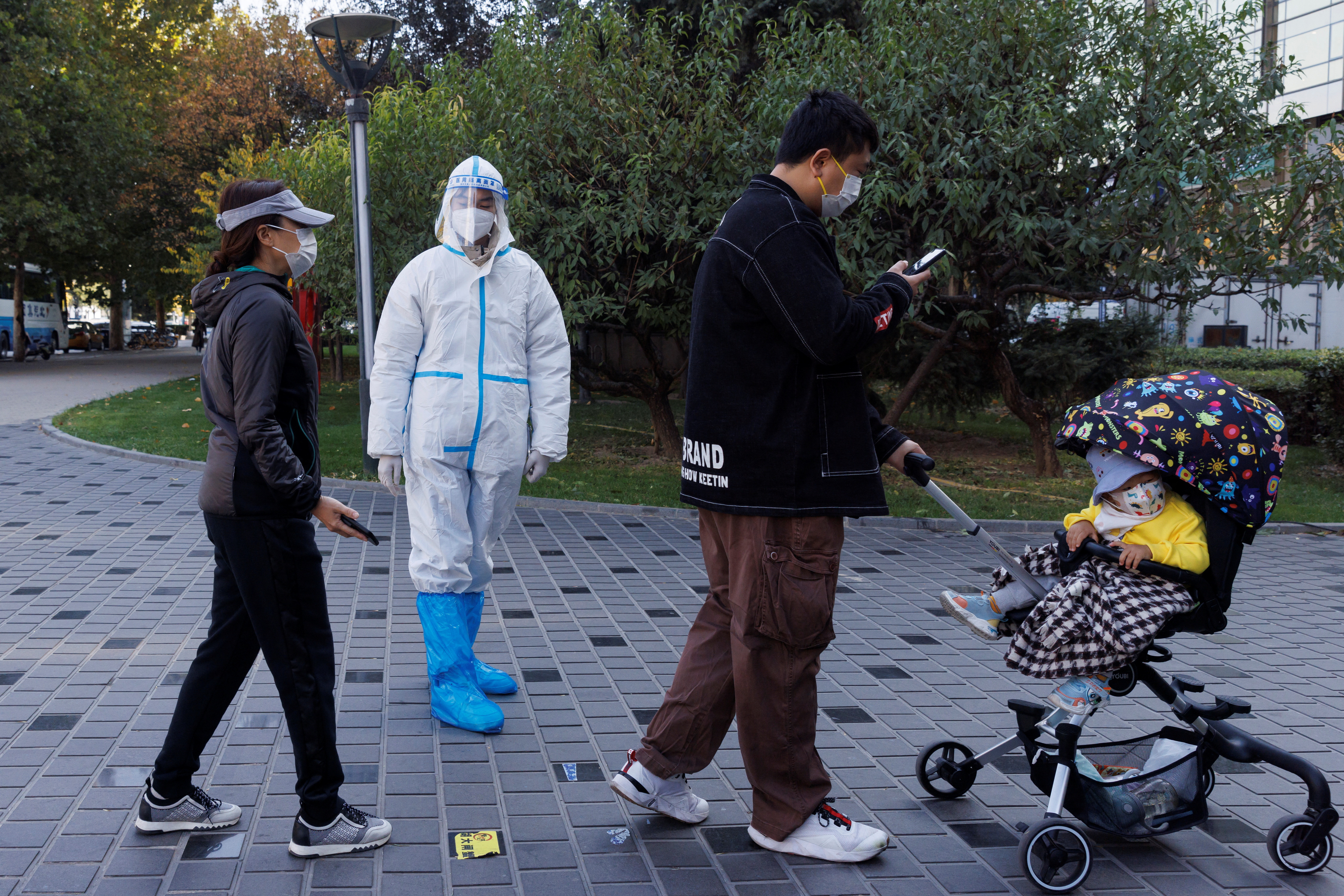 A pandemic prevention worker wears a protective suit as people line up to get swab tests at a testing booth as outbreaks of coronavirus disease (COVID-19) continue in Beijing