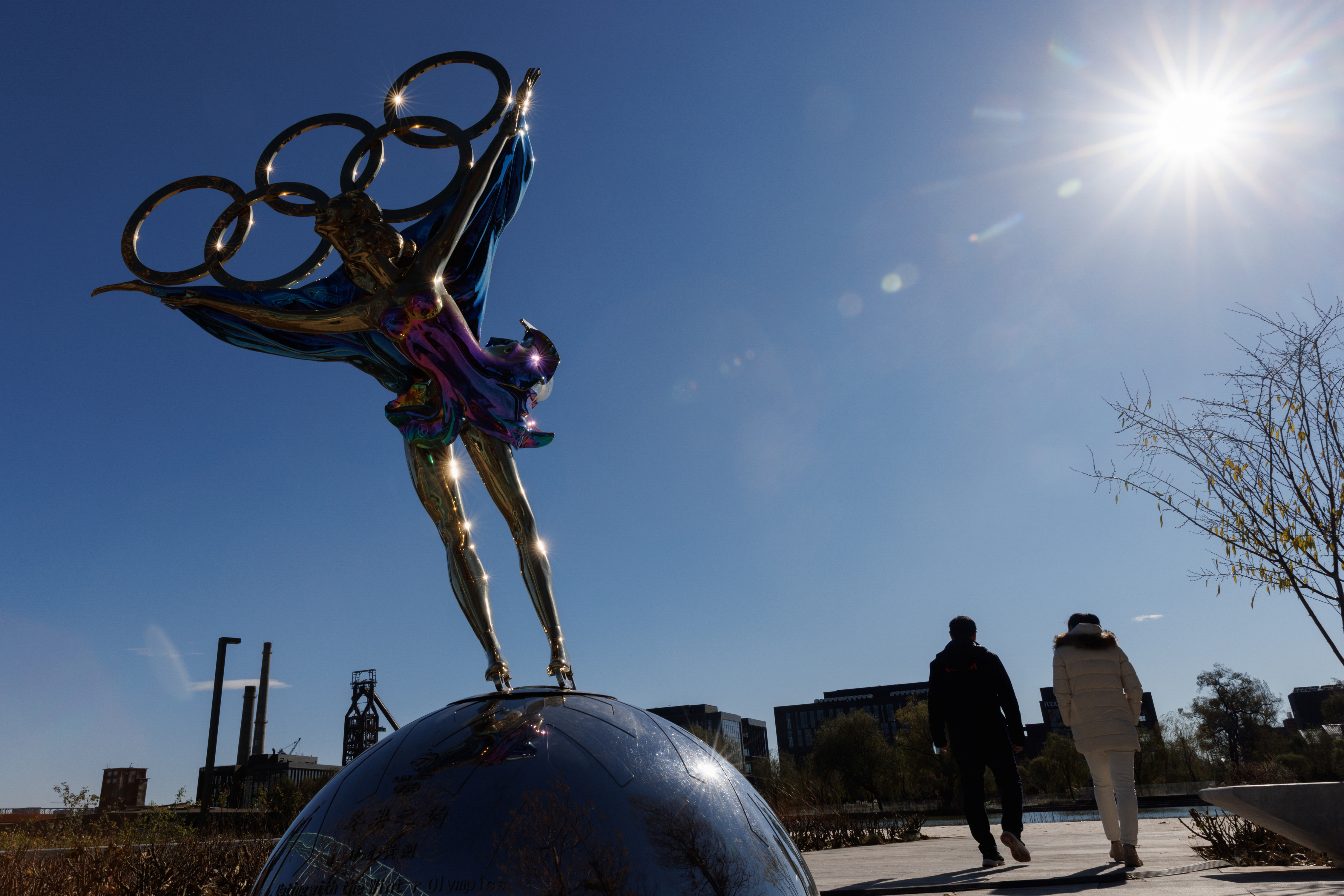 People walk past a sculpture featuring the Olympic rings outside the headquarters of the Beijing Organising Committee for the 2022 Olympic and Paralympic Winter Games in Shougang Park in Beijing