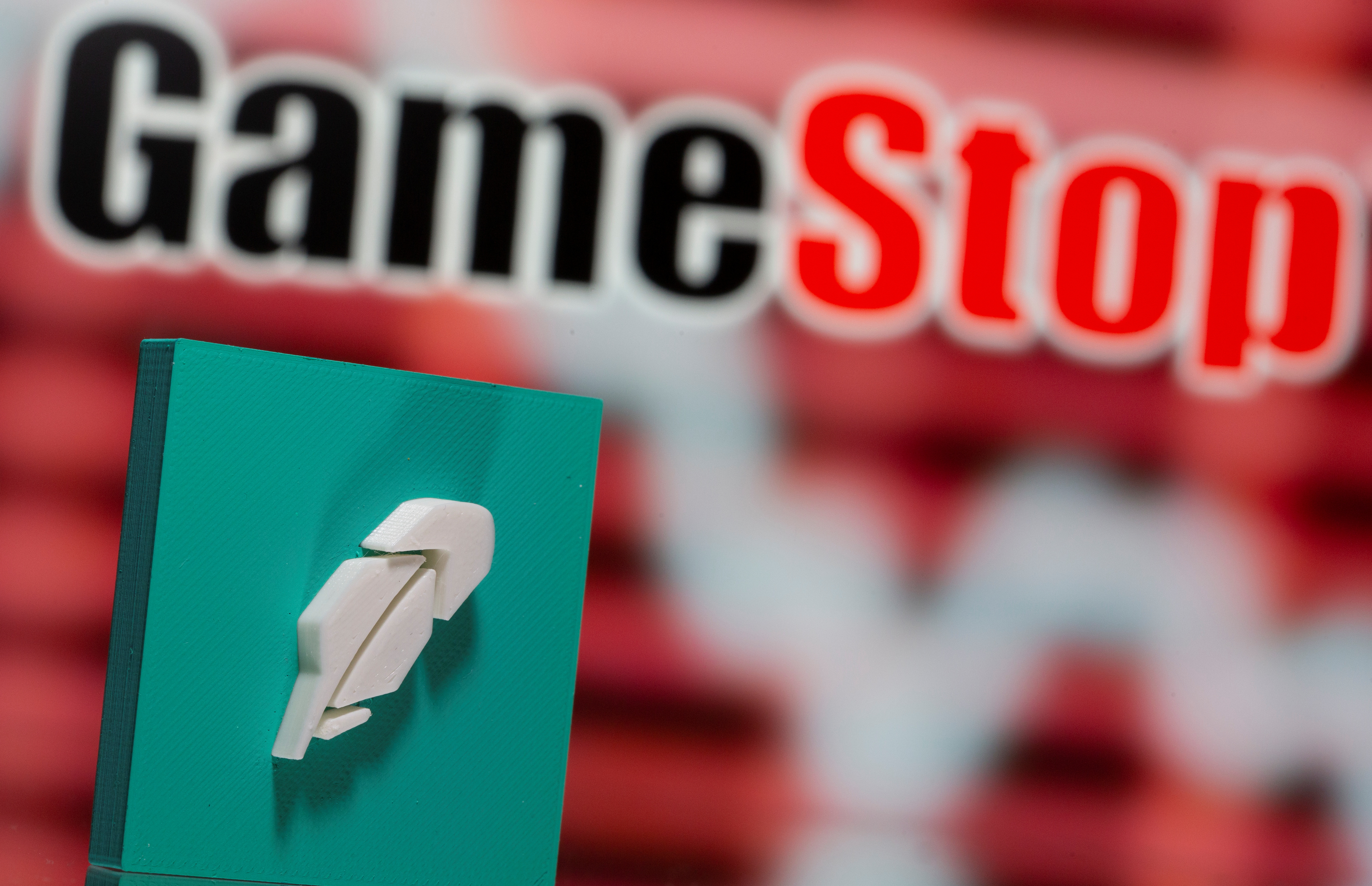 A 3d printed Robinhood logo is seen in front of displayed GameStop logo in this illustration