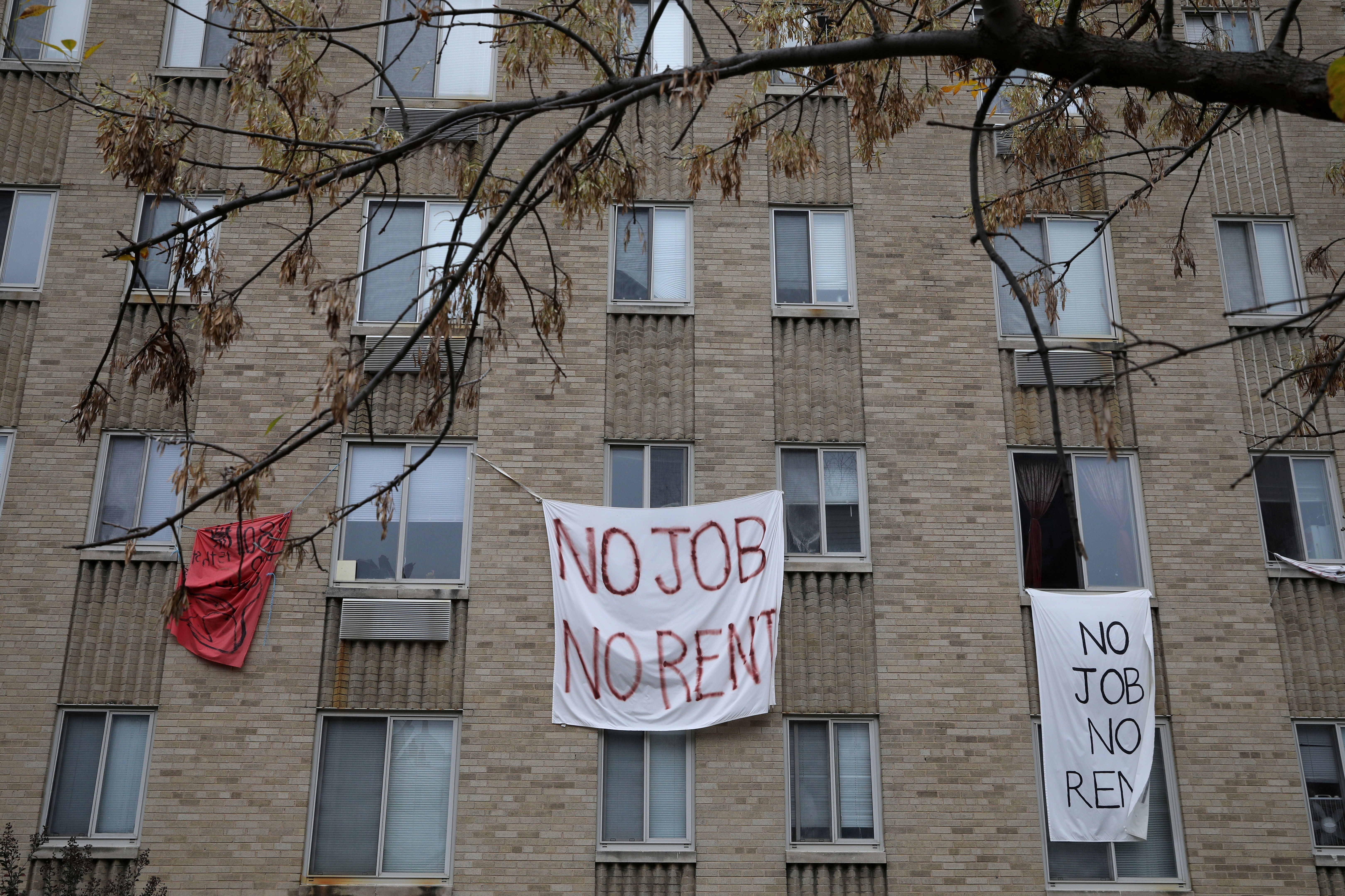 Makeshift sheets displaying messages of protest contesting the ability to pay for rent hang in a window of an apartment building in Washington