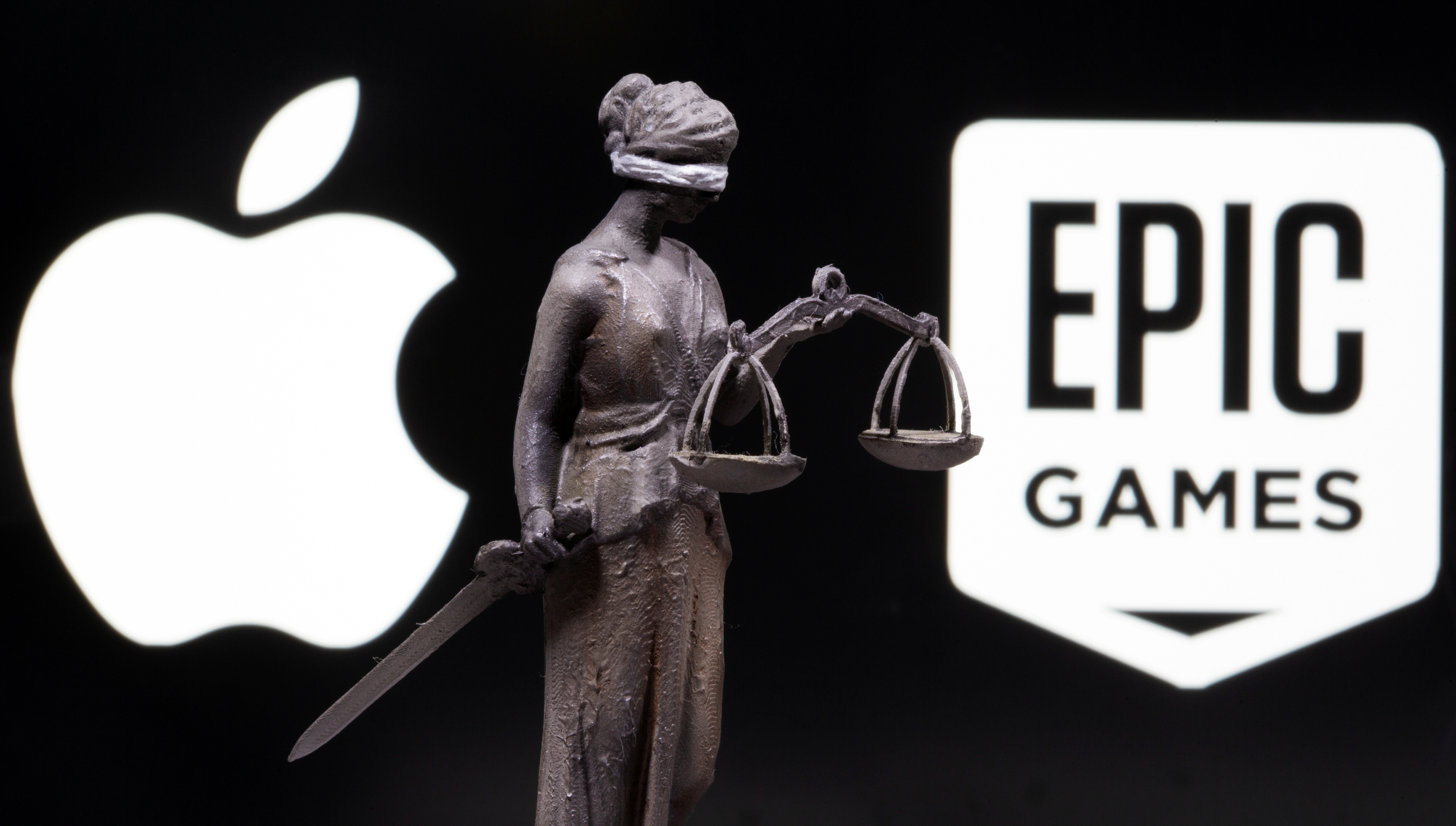 3D printed Lady Justice figure is seen in front of displayed Apple and Epic Games logos in this illustration photo