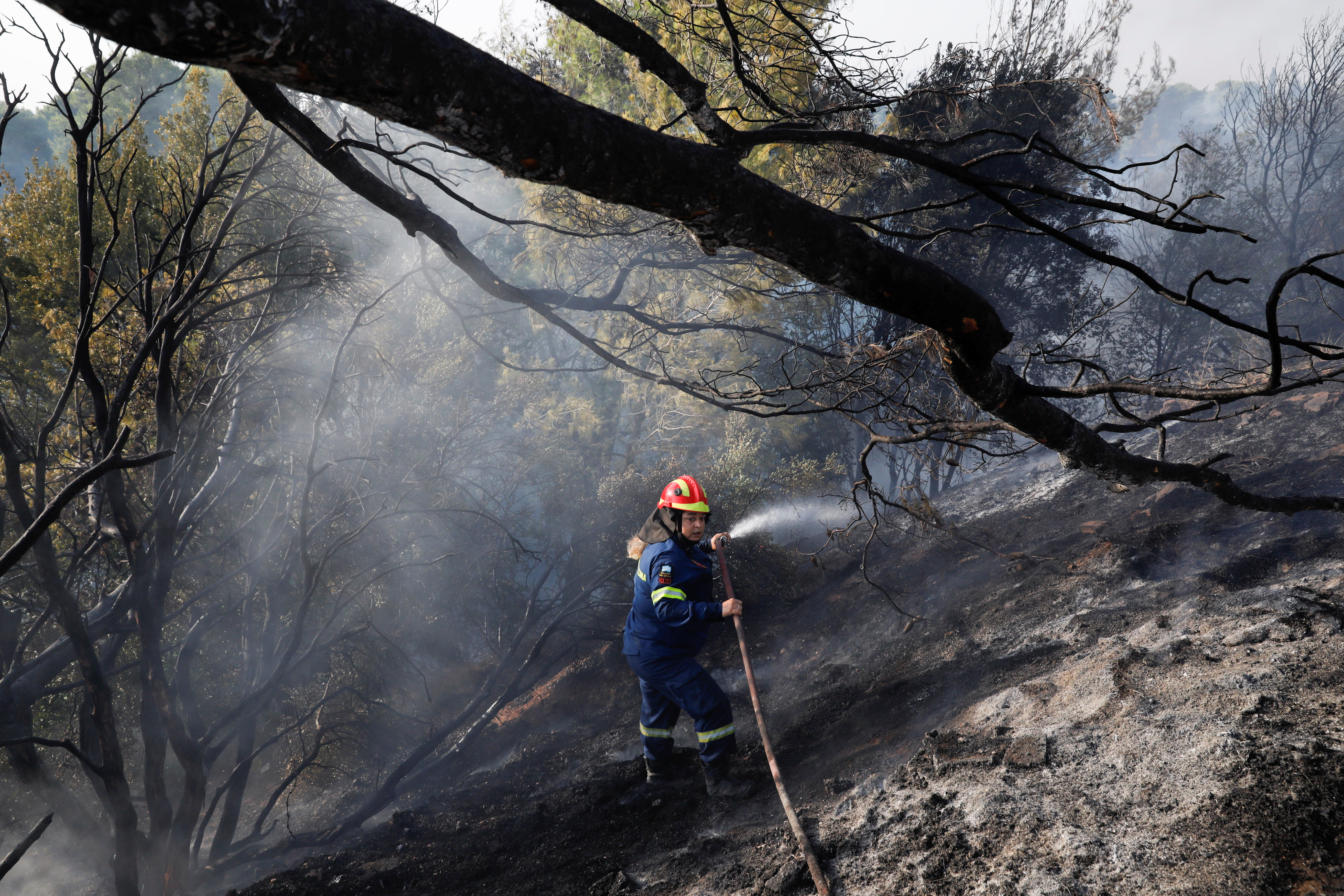Gasilec brizga vodo, da bi pomagal pri požaru v predmestju Varympompi severno od Aten v Grčiji, 4. avgusta 2021. REUTERS/Costas Baltas
