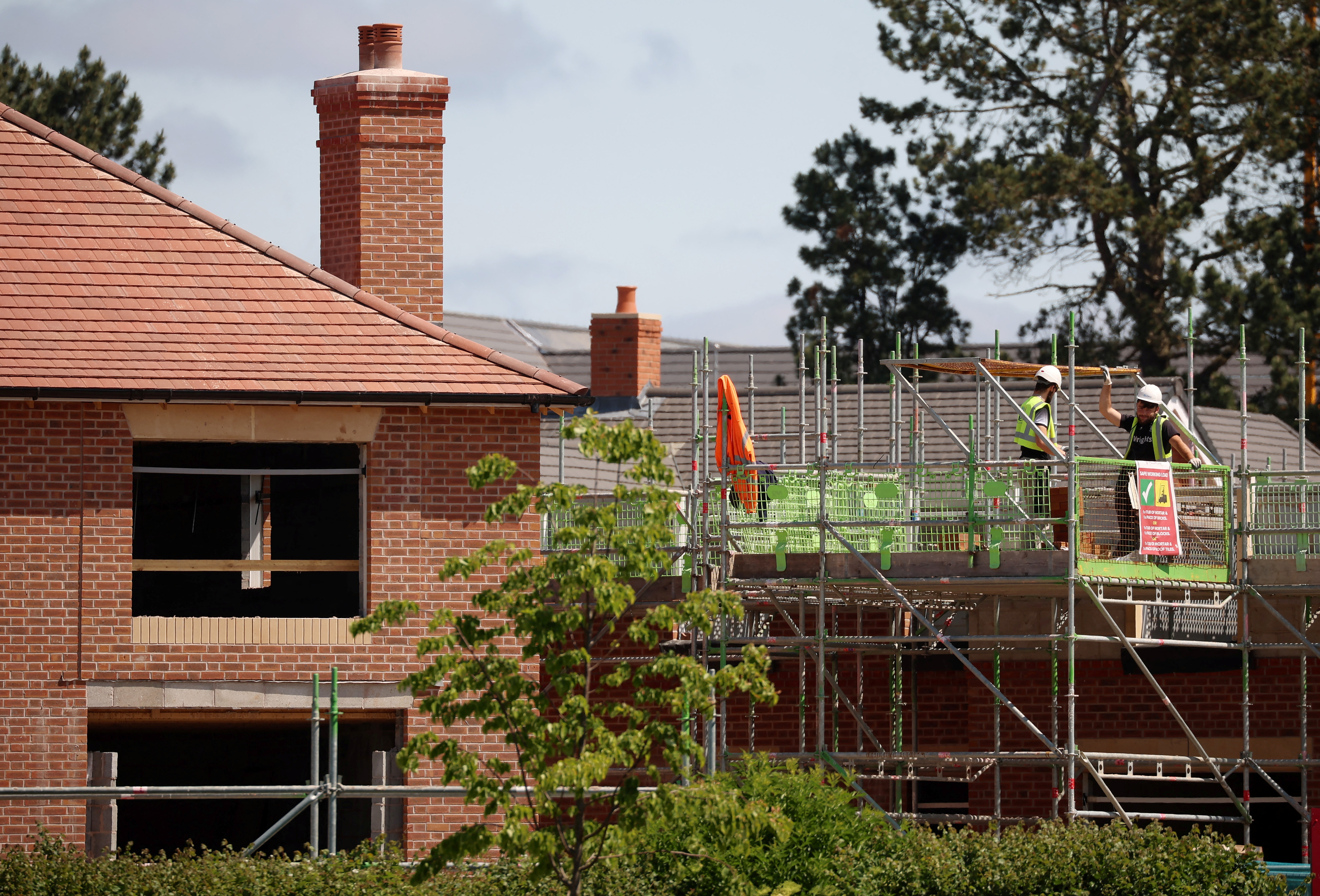 A construction worker stands on a scaffold platform on a new housing development under construction in Knutsford, Britain