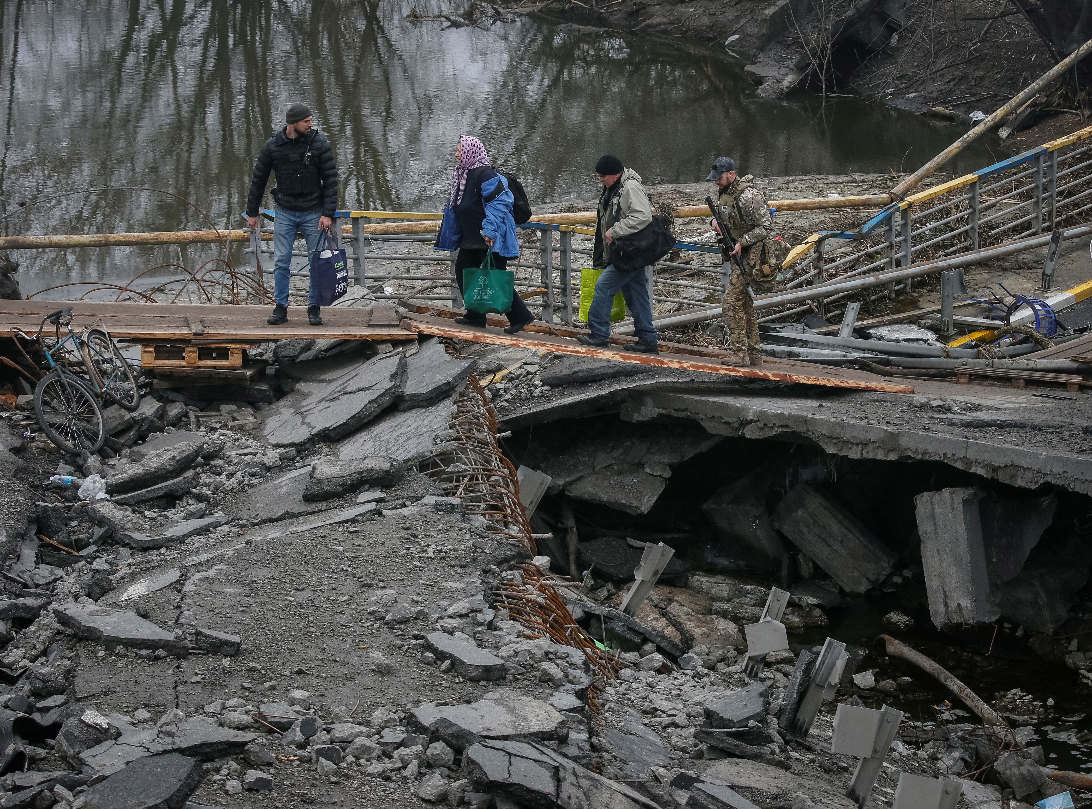 People cross the Irpin river near a destroyed bridge as they evacuate from Irpin town, amid Russia's invasion of Ukraine, outside of Kyiv