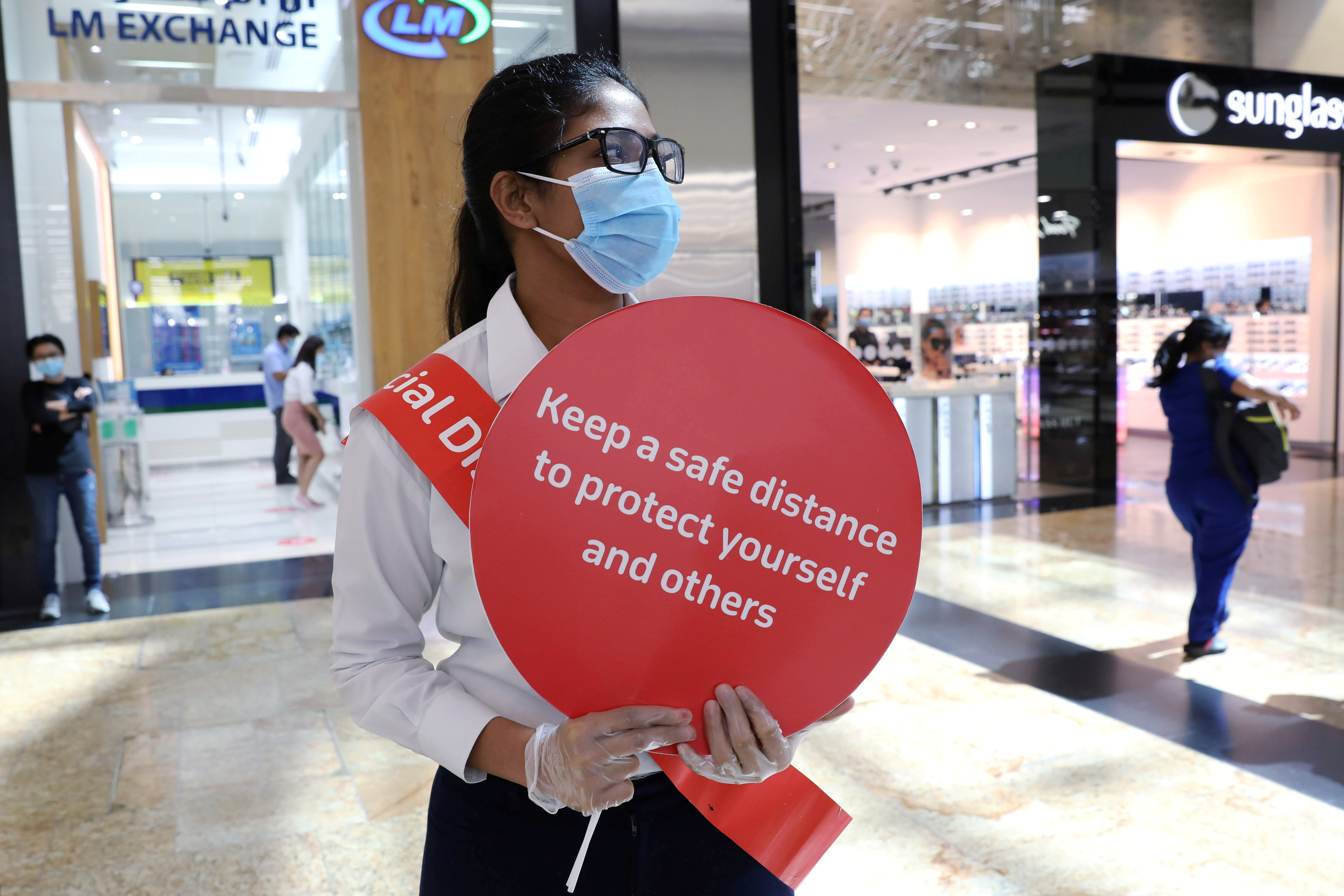 A woman wearing a protective face mask and gloves holds a sign at Mall of the Emirates in Dubai