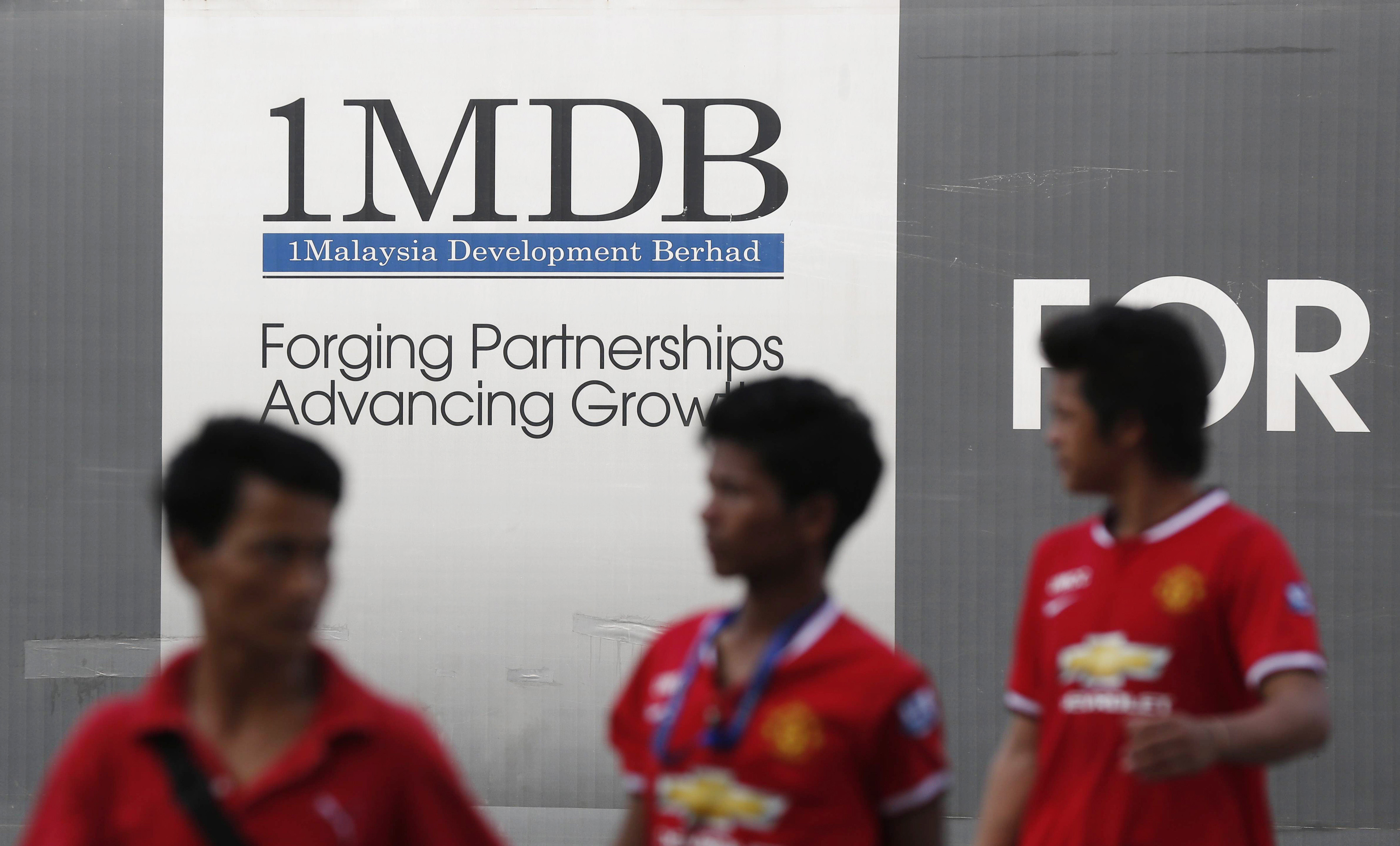 Men walk past a 1 Malaysia Development Berhad (1MDB) billboard at the funds flagship Tun Razak Exchange development in Kuala Lumpur