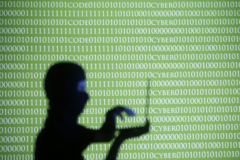   A person wearing a balaclava is silhouetted as he poses with a laptop in front of a screen projected with the word 'cyber' and binary code, in this picture illustration taken in Zenica October 29, 2014.     REUTERS/Dado Ruvic/File photo