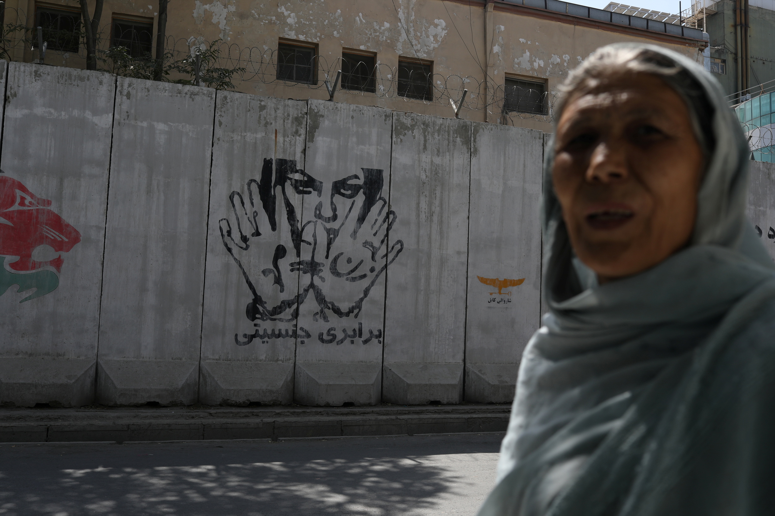 A mural reading "gender equality" is seen behind a woman in Kabul