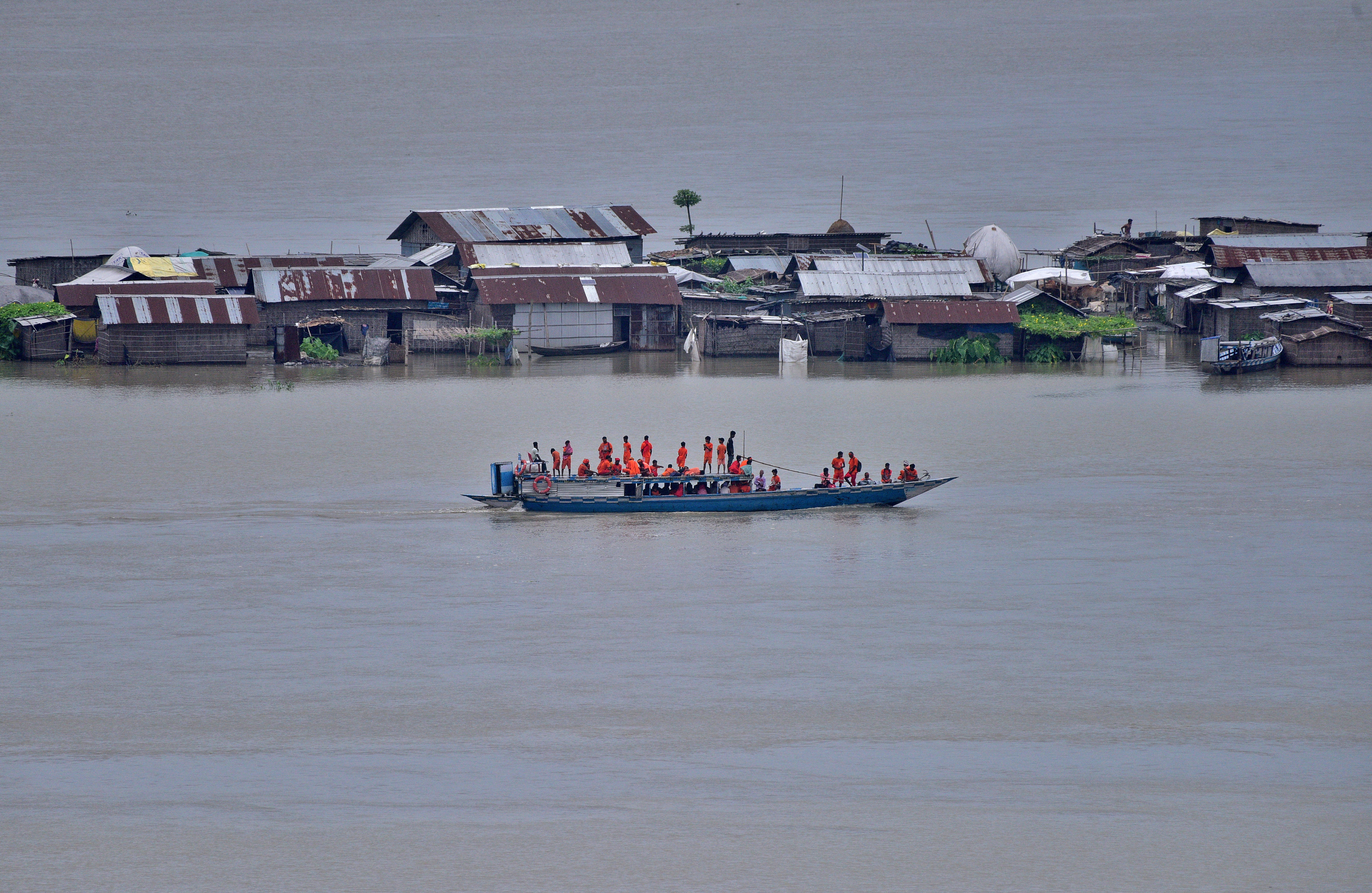 Kanwarias sail a boat past partially submerged houses at a flood-affected village in Morigaon district