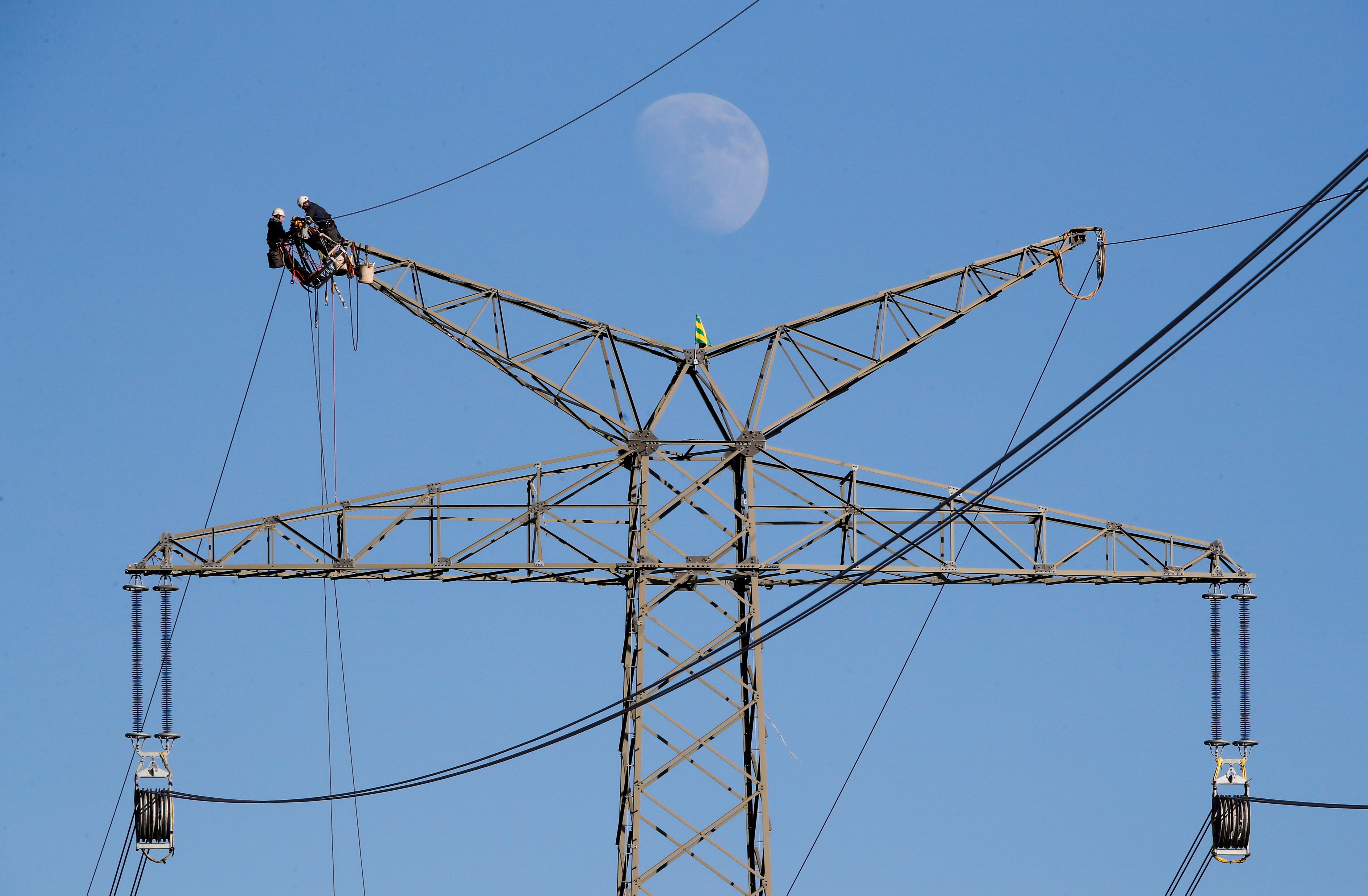 The moon rises as electricians work atop a power pole near the lignite power plant of Neurath of German energy supplier and utility RWE, near Rommerskirchen