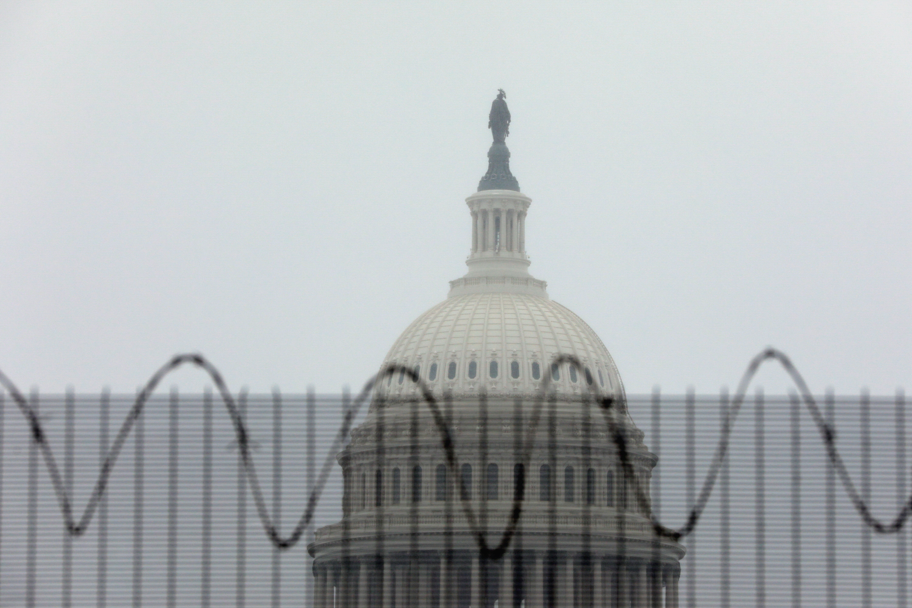 The U.S. Capitol dome is seen behind protective fencing as it snows in Washington