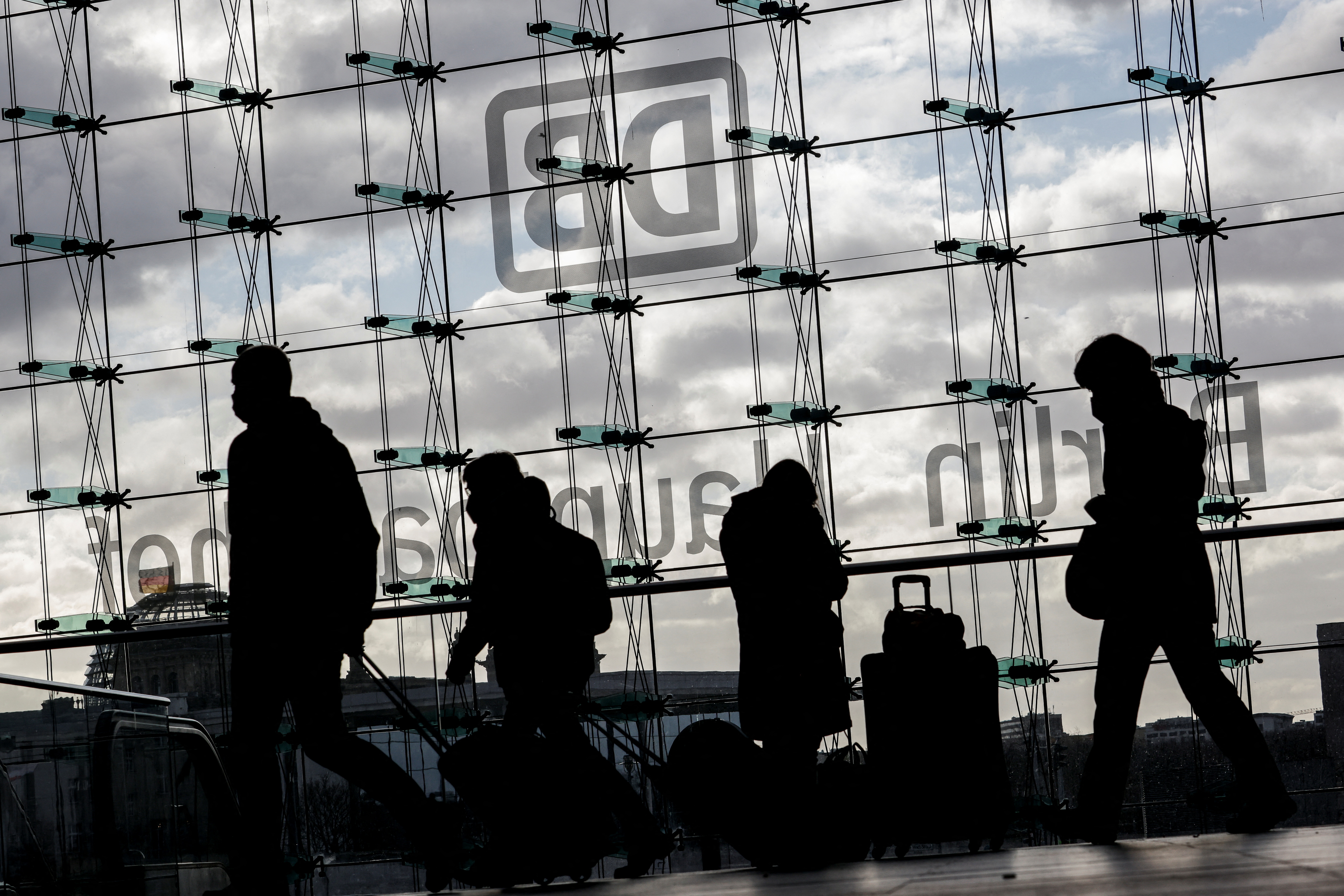 Commuters are silhouetted against a cloudy sky at the DB Berlin Hauptbahnhof or the main train station in Berlin