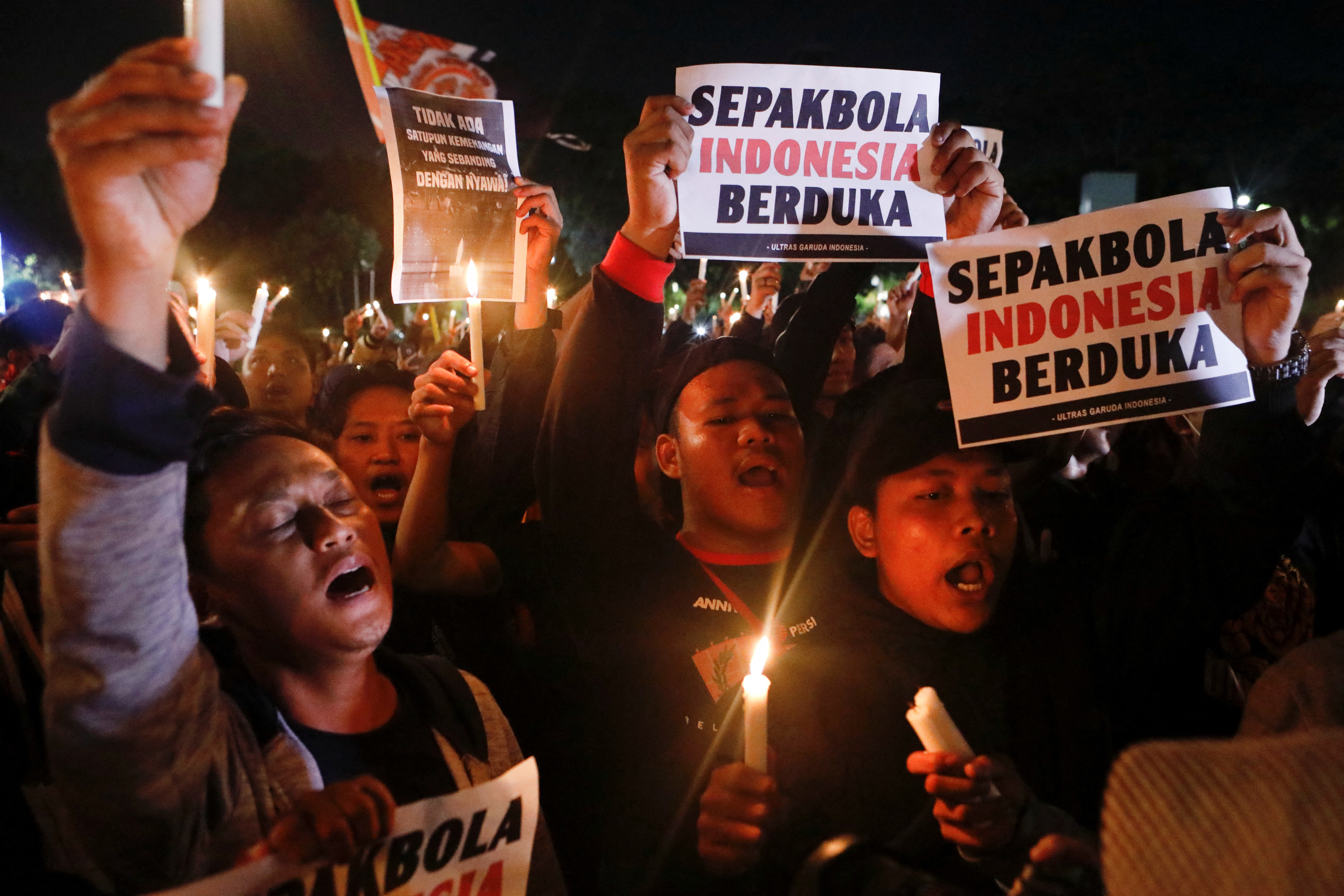 Football fans hold candles and placards during a vigil at Gelora Bung Karno Stadium area, following a riot after the football match between Arema vs Persebaya in Jakarta